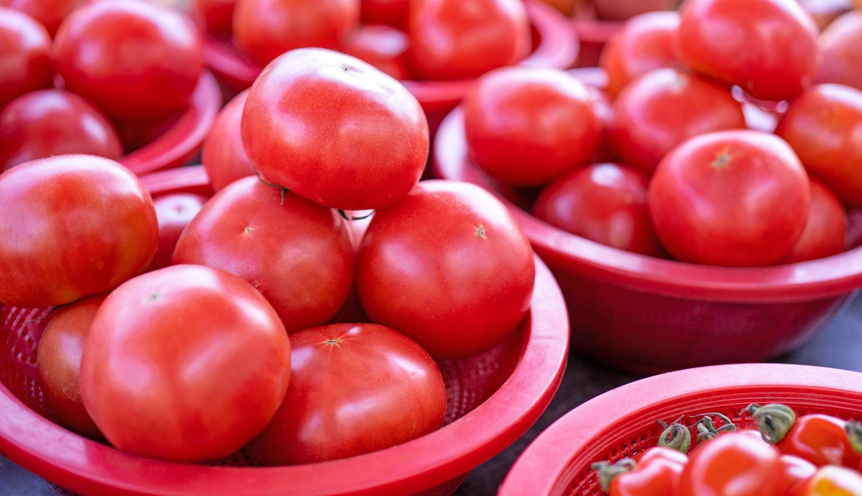 läckra färska tomater frukt grönsaksmat i röd plastkorg på traditionsmarknadseftermiddag, seoul, Sydkorea, skördekoncept, närbild. foto