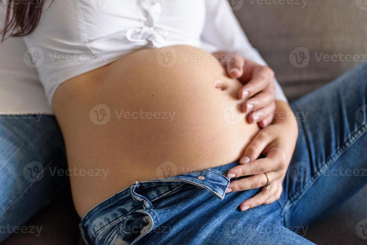 en man och en gravid kvinna sitter och kramas i soffan. foto