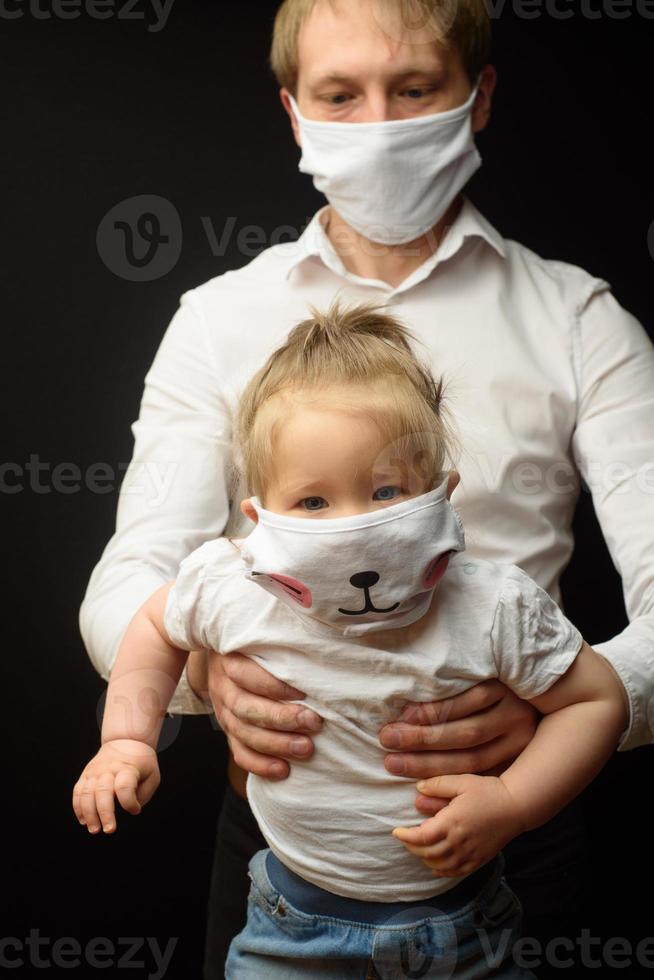 pappa i en medicinsk mask håller sin lilla dotter. konceptet att skydda barn under epidemin av coronavirus foto