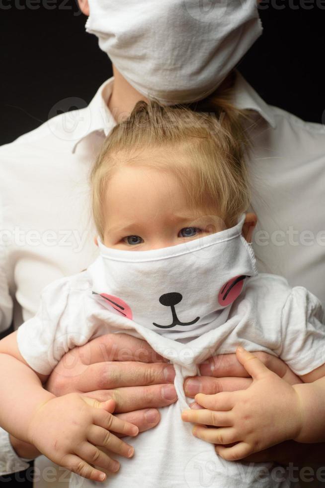 pappa i en medicinsk mask håller sin lilla dotter. konceptet att skydda barn under epidemin av coronavirus foto