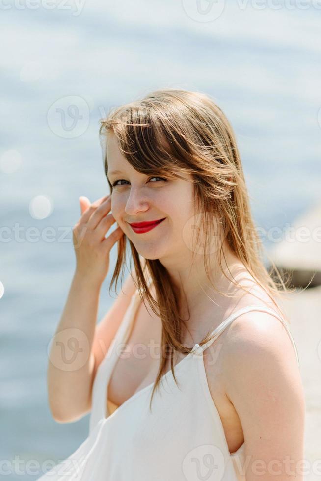 en ung vacker flicka i en lång mjölkfärgad klänning går längs stranden och piren mot havets bakgrund. foto