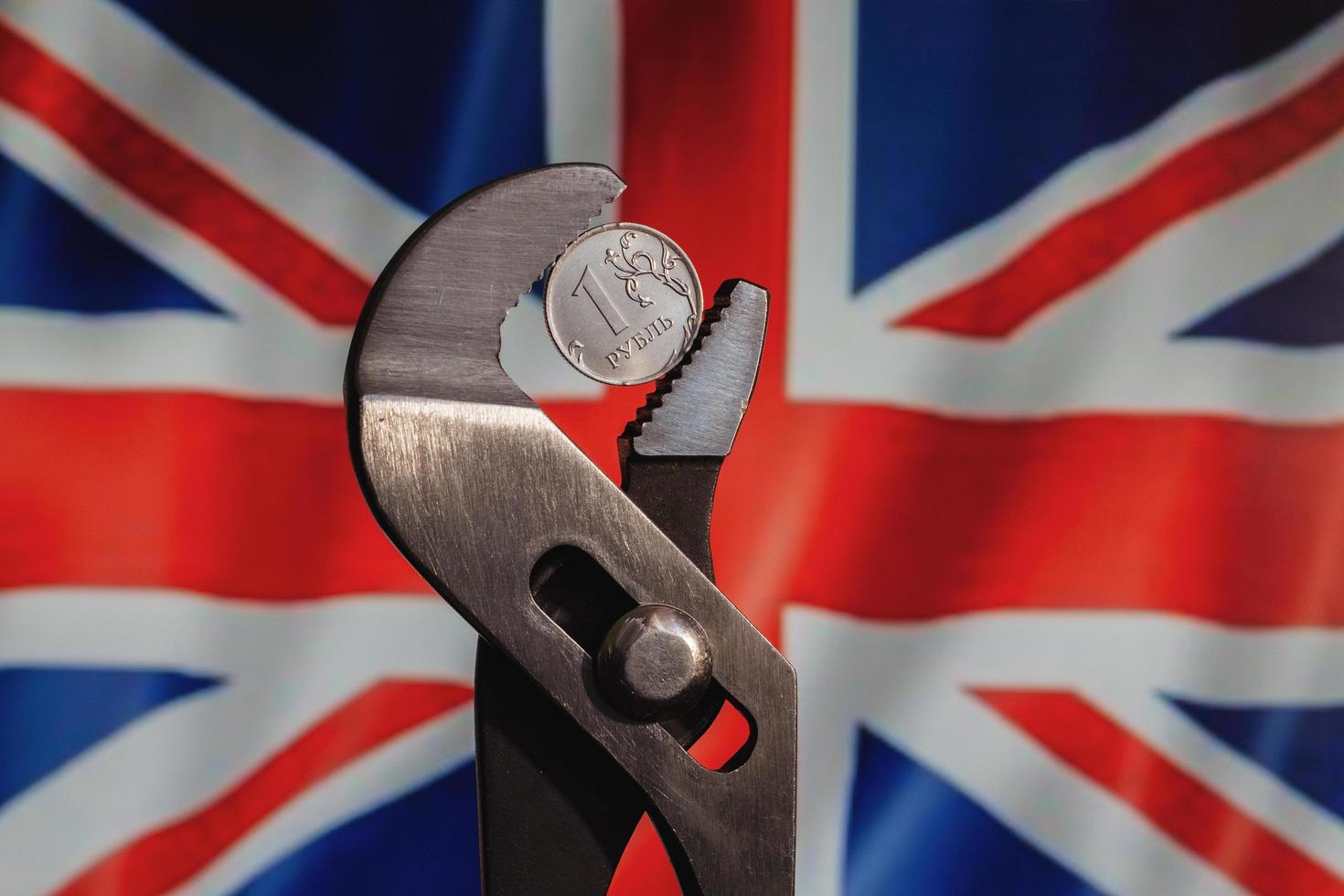 mynt en rubel är fastklämd i en skiftnyckel mot bakgrunden av Storbritanniens flagga. idén om rubelns kollaps och ekonomiska sanktioner mot Ryssland. foto