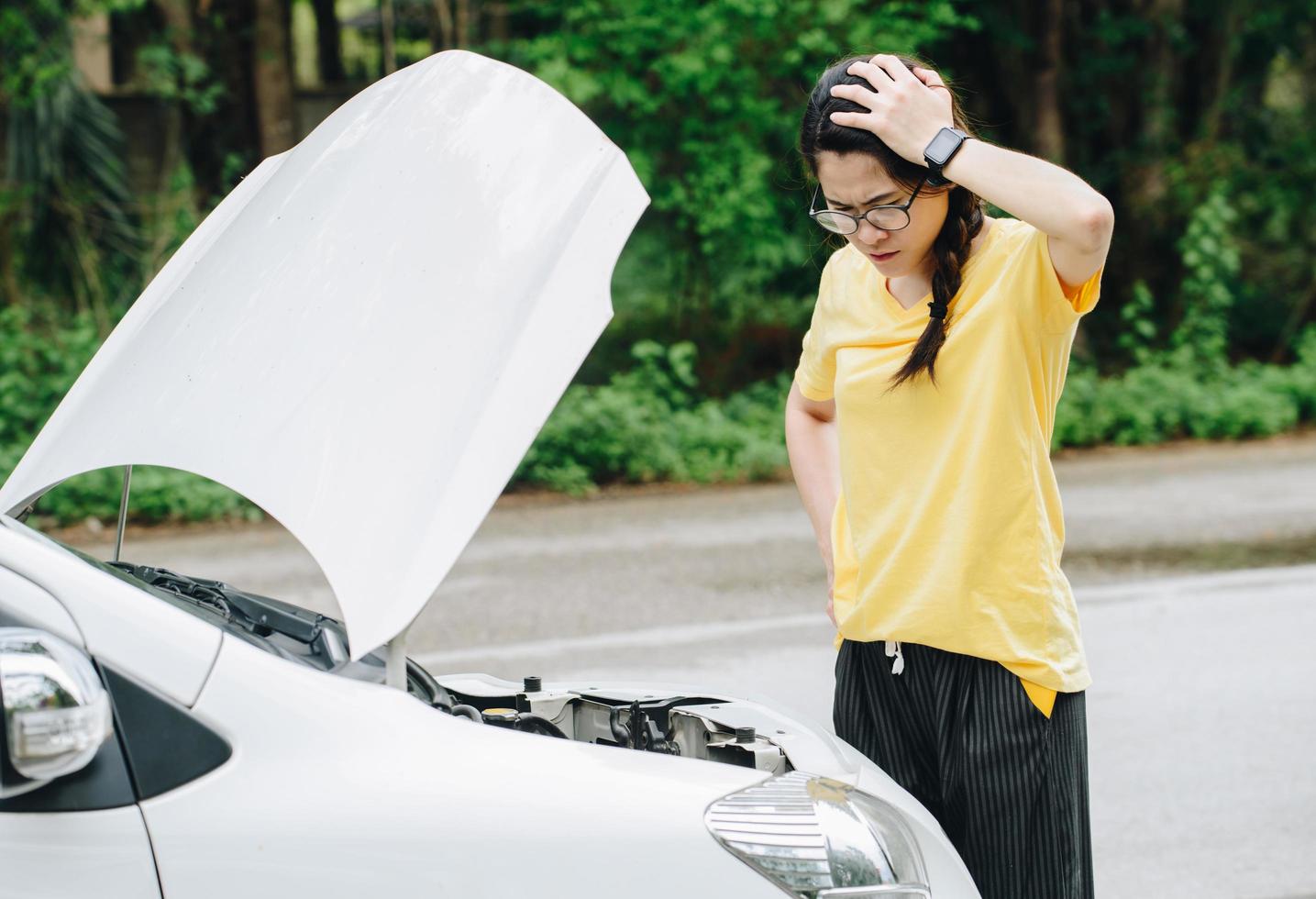 asiatisk kvinna öppnade bilhuven för att se problemet med bilhaveri medan hon väntade på hjälp på vägkanten. bilhaveri det kommer att hända dig minst en gång under ditt körliv. foto