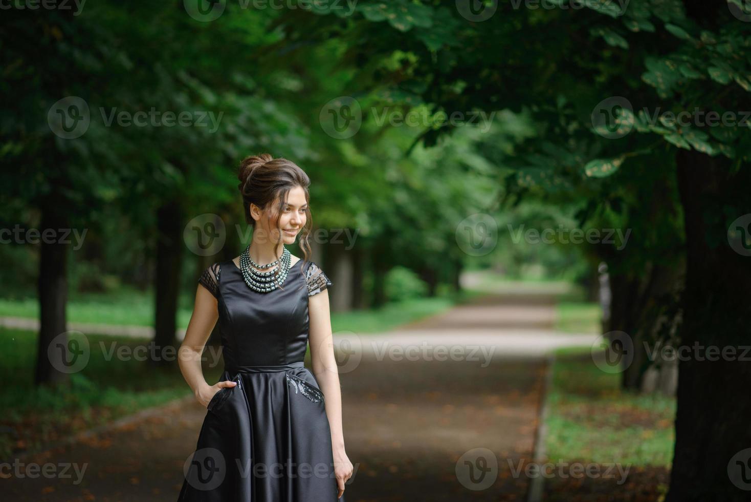 ung vacker kvinna poserar i en svart klänning i en park. foto