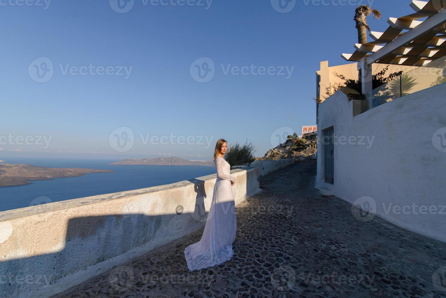 vacker brud i en vit klänning poserar mot bakgrunden av Medelhavet i Thira, Santorini. foto