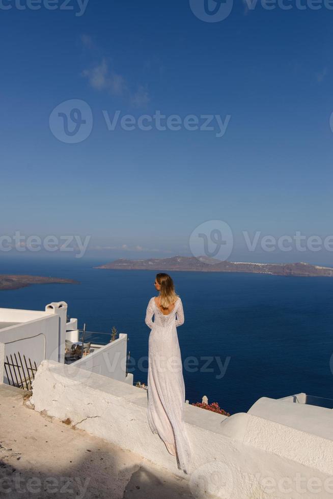 vacker brud i en vit klänning poserar mot bakgrunden av Medelhavet i Thira, Santorini. foto