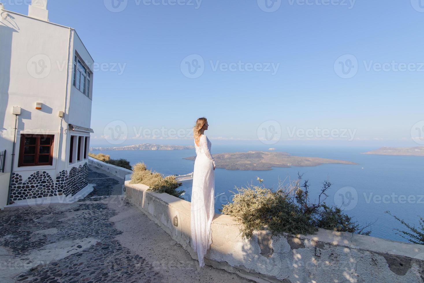 vacker brud i en vit klänning poserar mot bakgrunden av Medelhavet i Thira, Santorini. foto