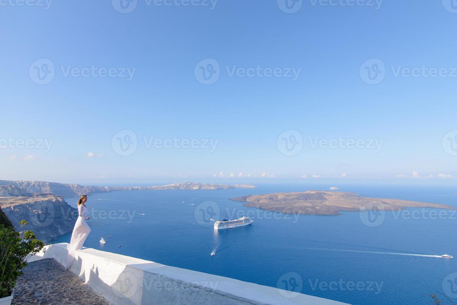 vacker brud i en vit klänning poserar mot bakgrunden av Medelhavet i Thira, Santorini. foto