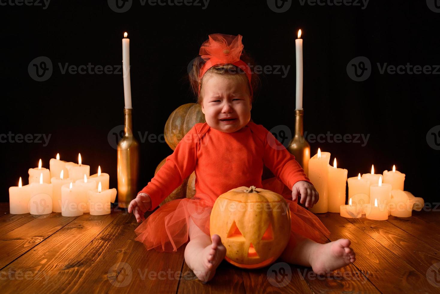 liten flicka sitter på en bakgrund av jack pumpor och ljus på en svart bakgrund. foto