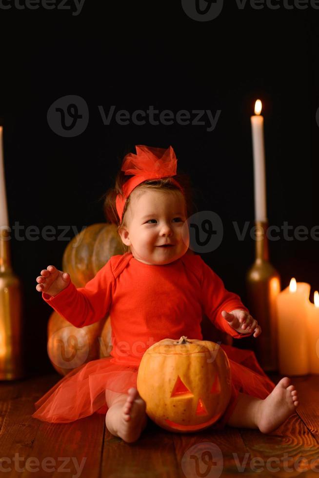 liten flicka sitter på en bakgrund av jack pumpor och ljus på en svart bakgrund. foto