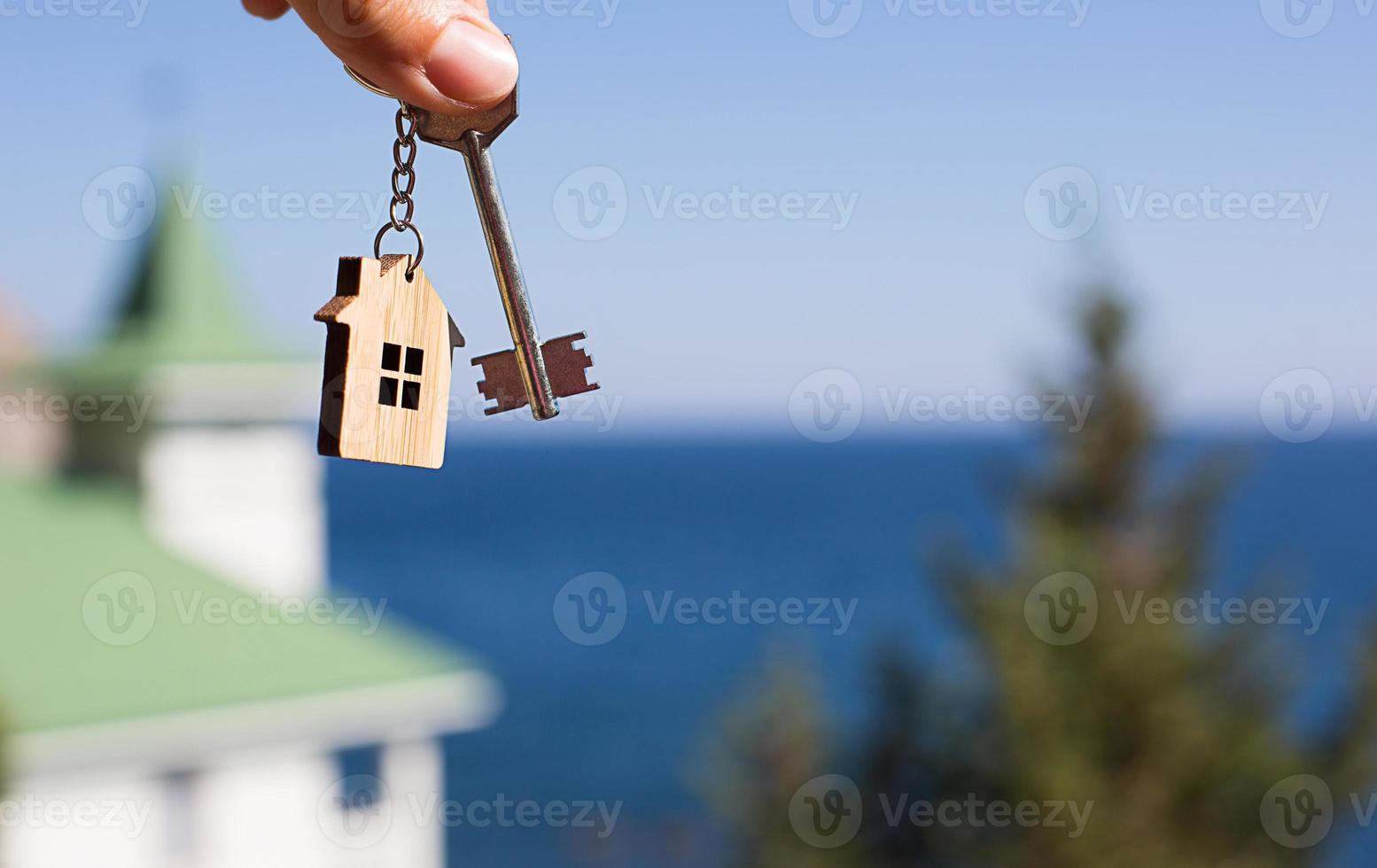 trähänge av ett hus och nyckel. bakgrund av havet, gran och stuga. hus och livet på havet, konstruktion, projekt, flytt till nytt hus, bolån, hyra och köp av fastighet. kopieringsutrymme foto