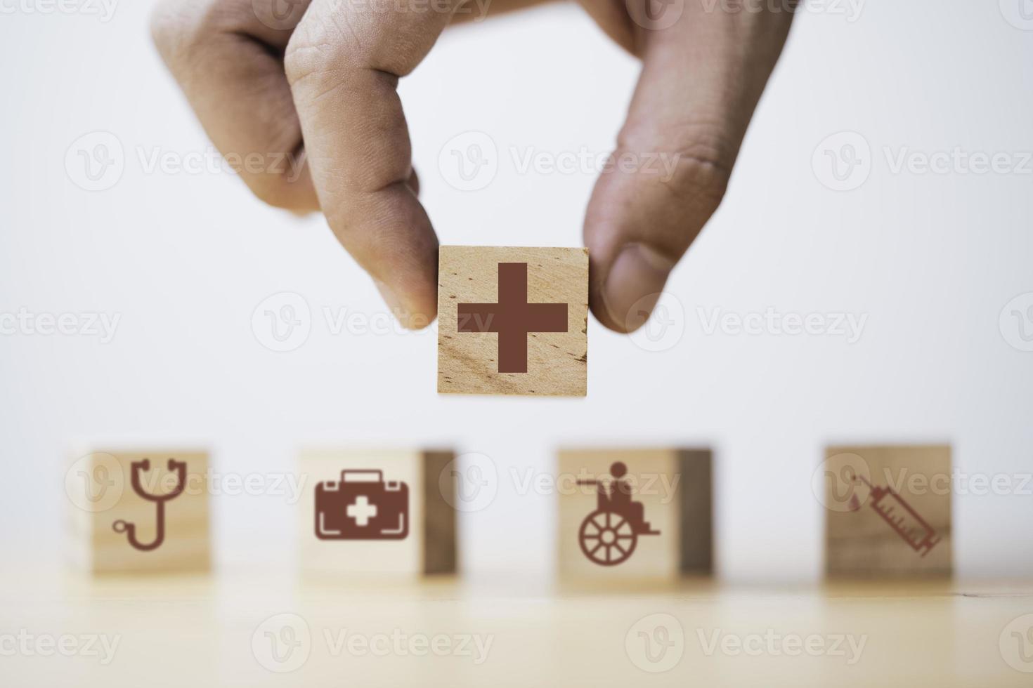 hand som håller hälsovård och medicinska ikoner utskriftsskärm på träblock för hälsosam välbefinnande försäkring och försäkran koncept. foto