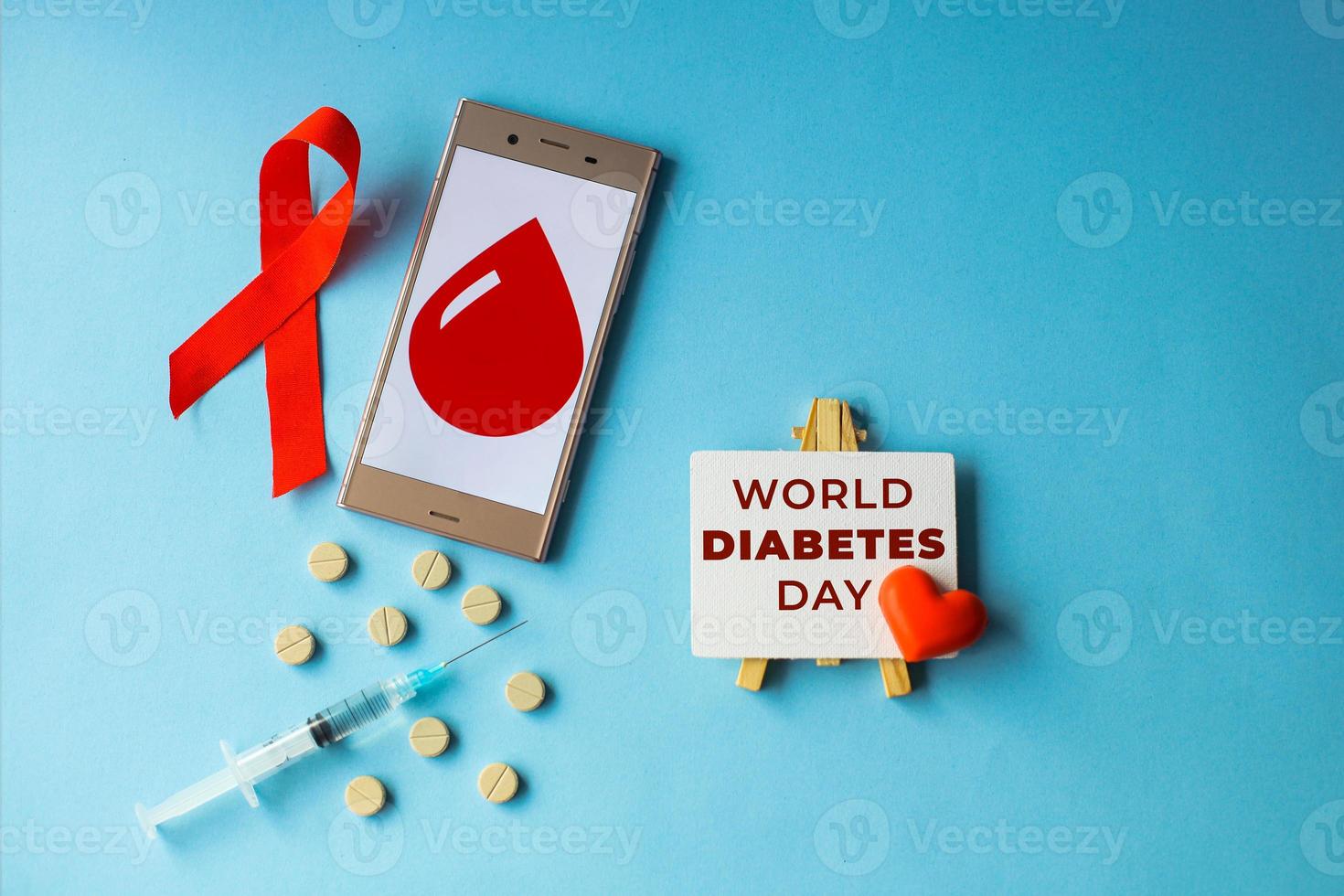 världens diabetes dag kreativa platt låg koncept med rött band, blodsymbol, droger och spruta på blå bakgrund foto