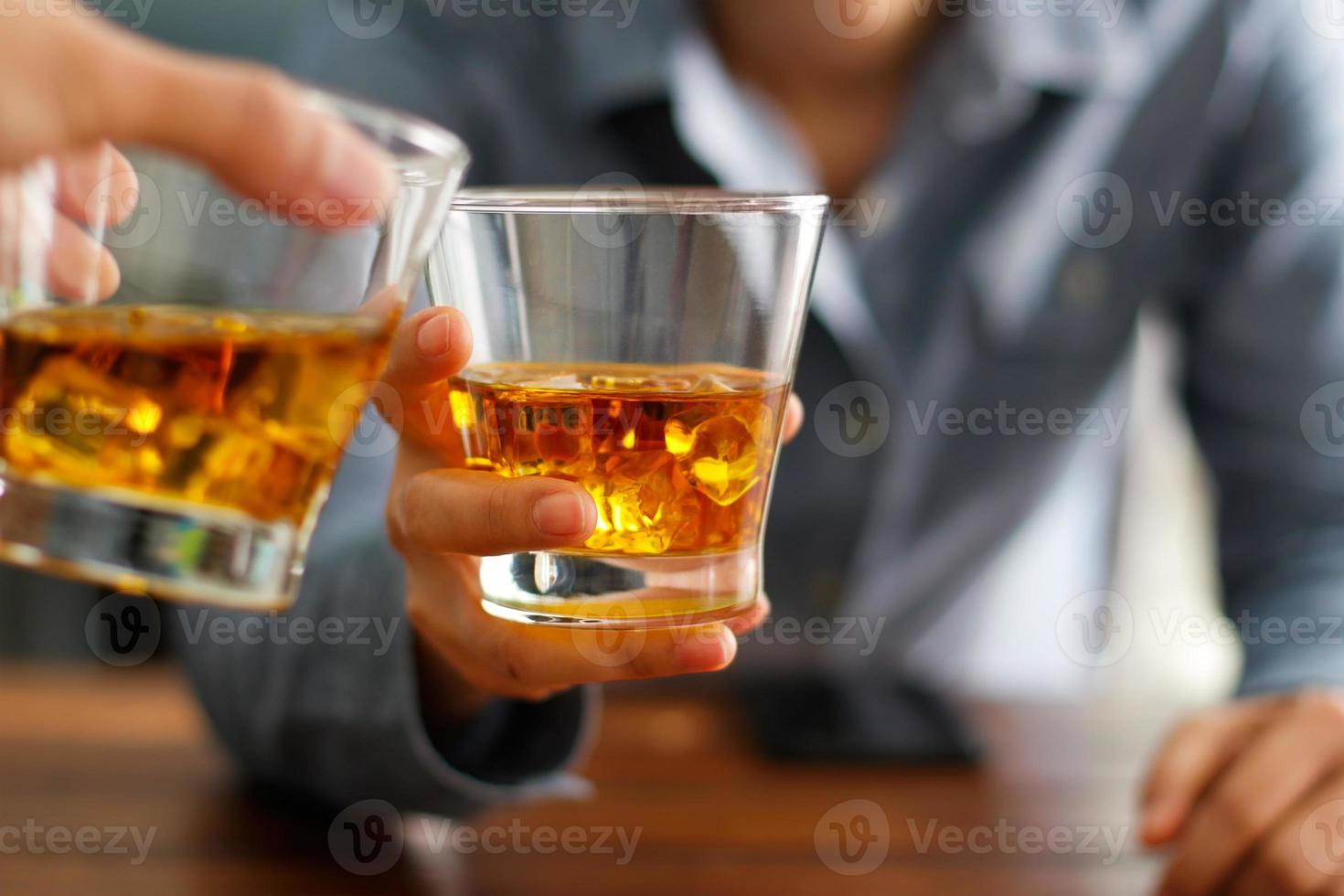 närbild av två män som klirrar i glas whisky dricker alkohol tillsammans medan de står vid bardisken på puben foto