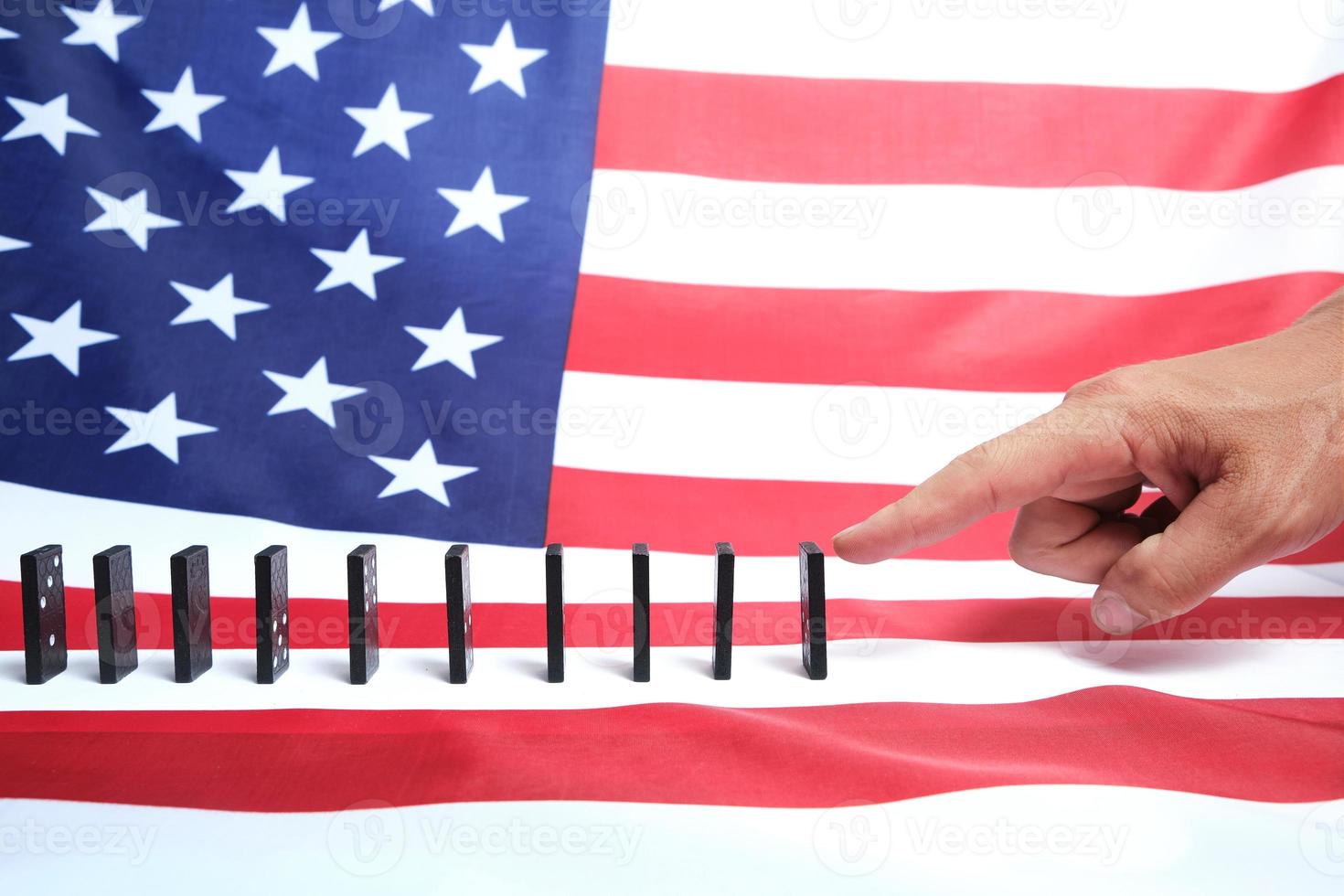 vit mans finger trycker en domino mot bakgrunden av den amerikanska flaggan. foto