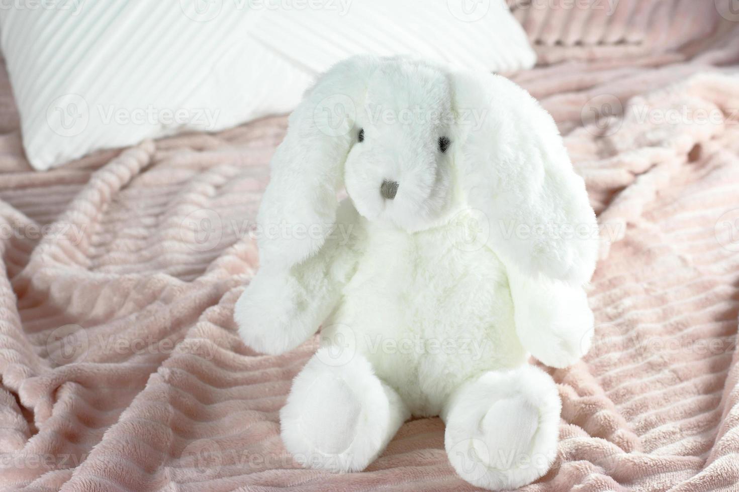vit fluffig kaninleksak på rosa filt, kanin sitter på sängen foto