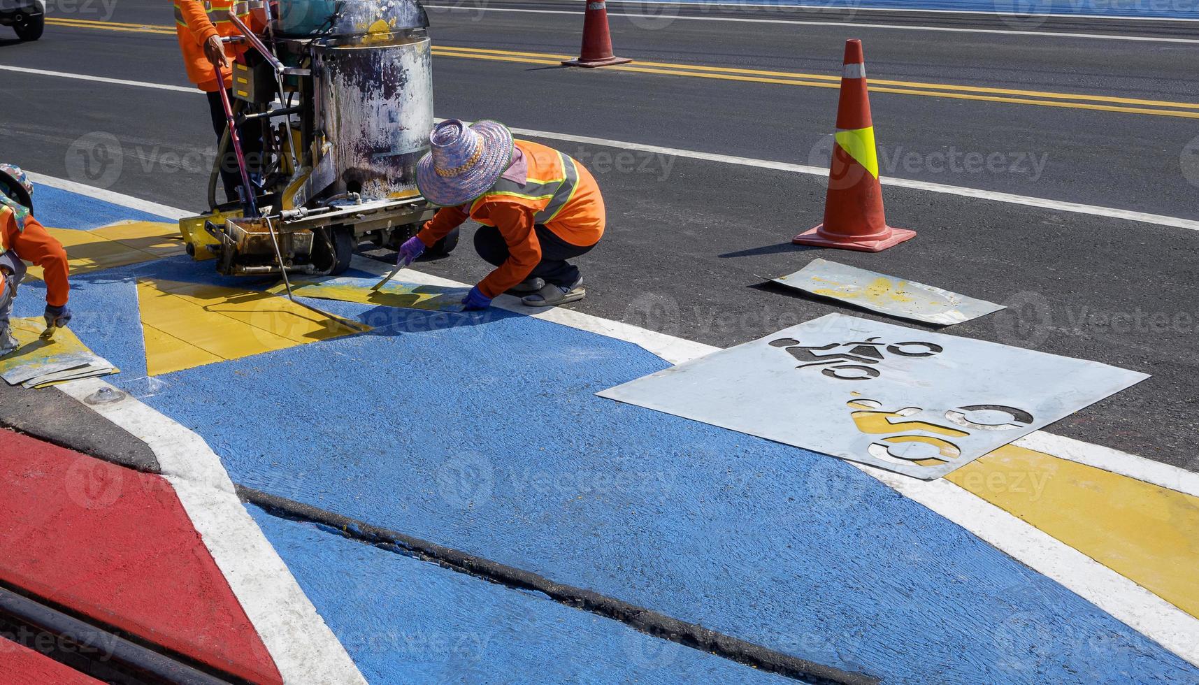vägarbetargrupp med termoplastsprayvägmarkeringsmaskin arbetar med att måla trafikskylt och cykelbana på asfaltväg med järnvägskorsning på gatuytan foto