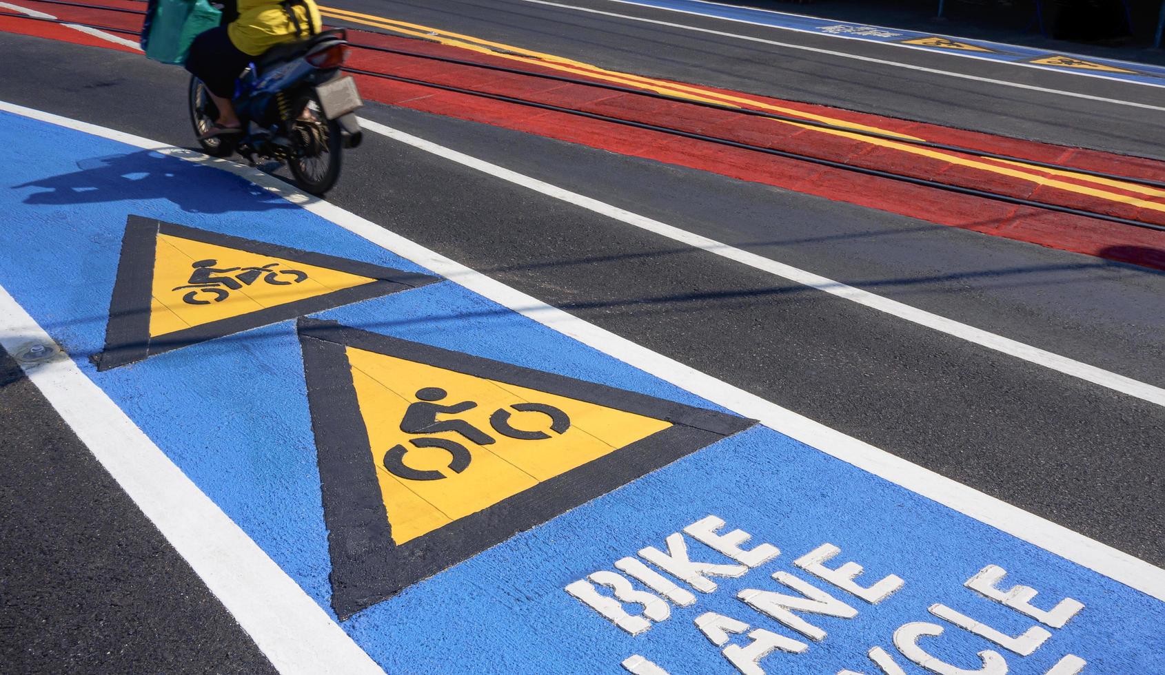 färgglad cykelvägskylt, pil och cykelbana text med rörelseoskärpa av motorcykel på asfaltsväg med järnvägskorsning på gatuytan, trafikskylt och symbolkoncept foto