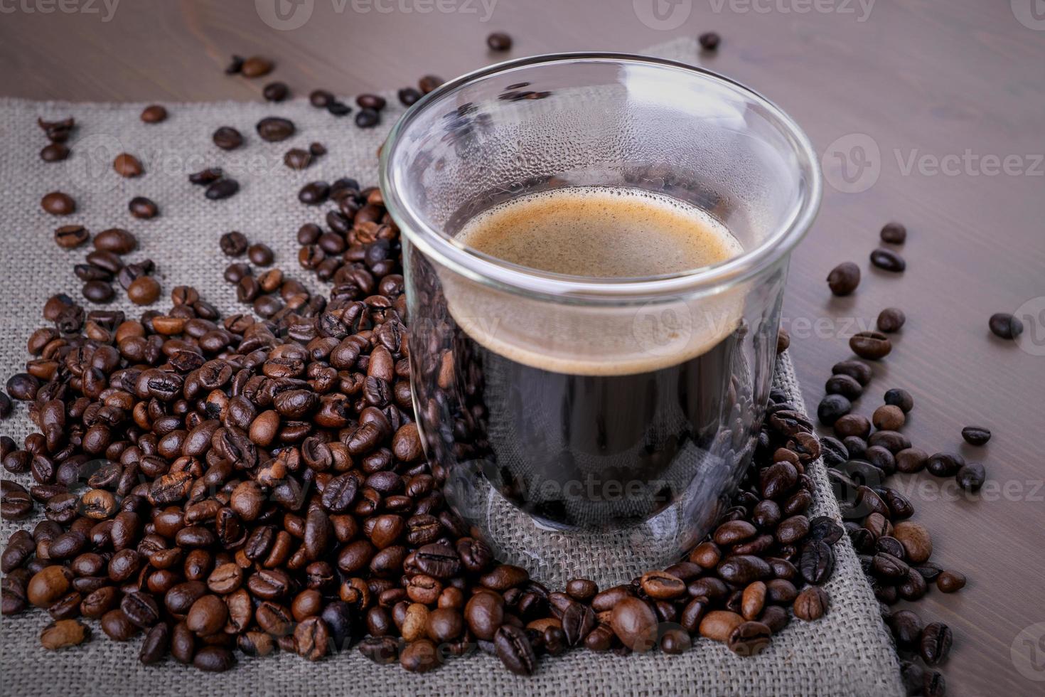 glaskopp med kaffe och hög med rostade kaffebönor foto