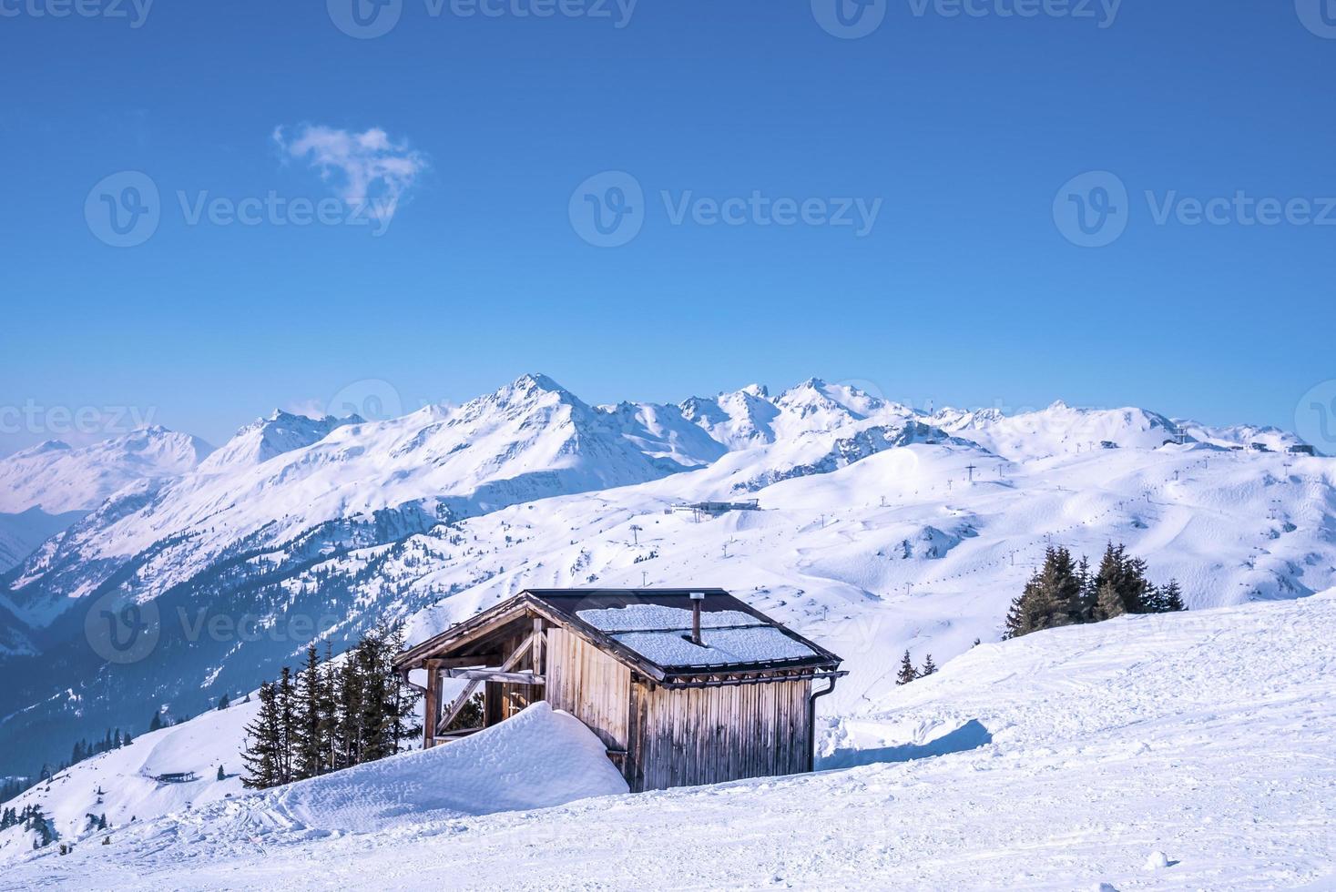 litet trähus på snöiga berg mot blå himmel foto