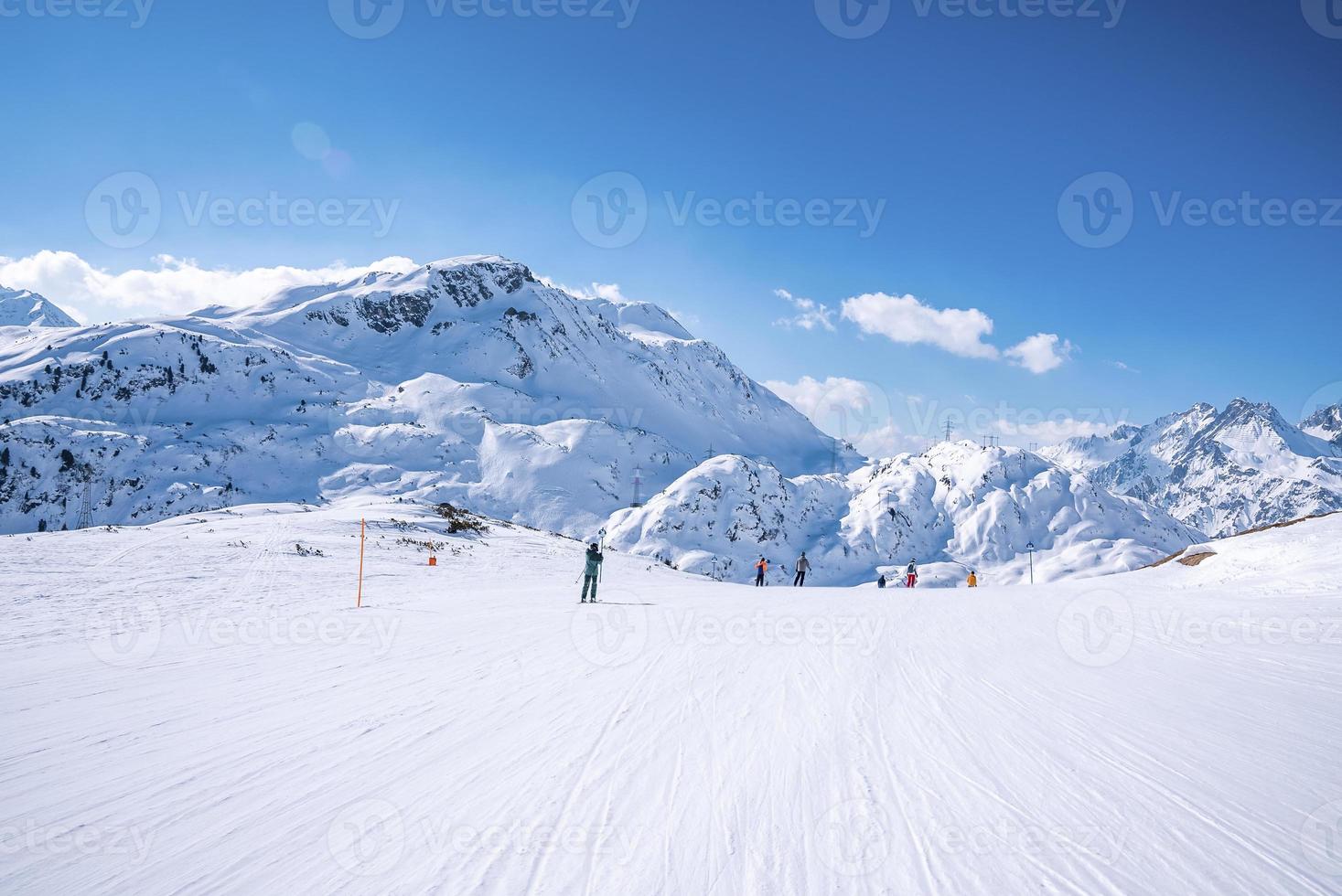 skidåkare i sportkläder åker skidor på snöig bergskedja mot himlen foto