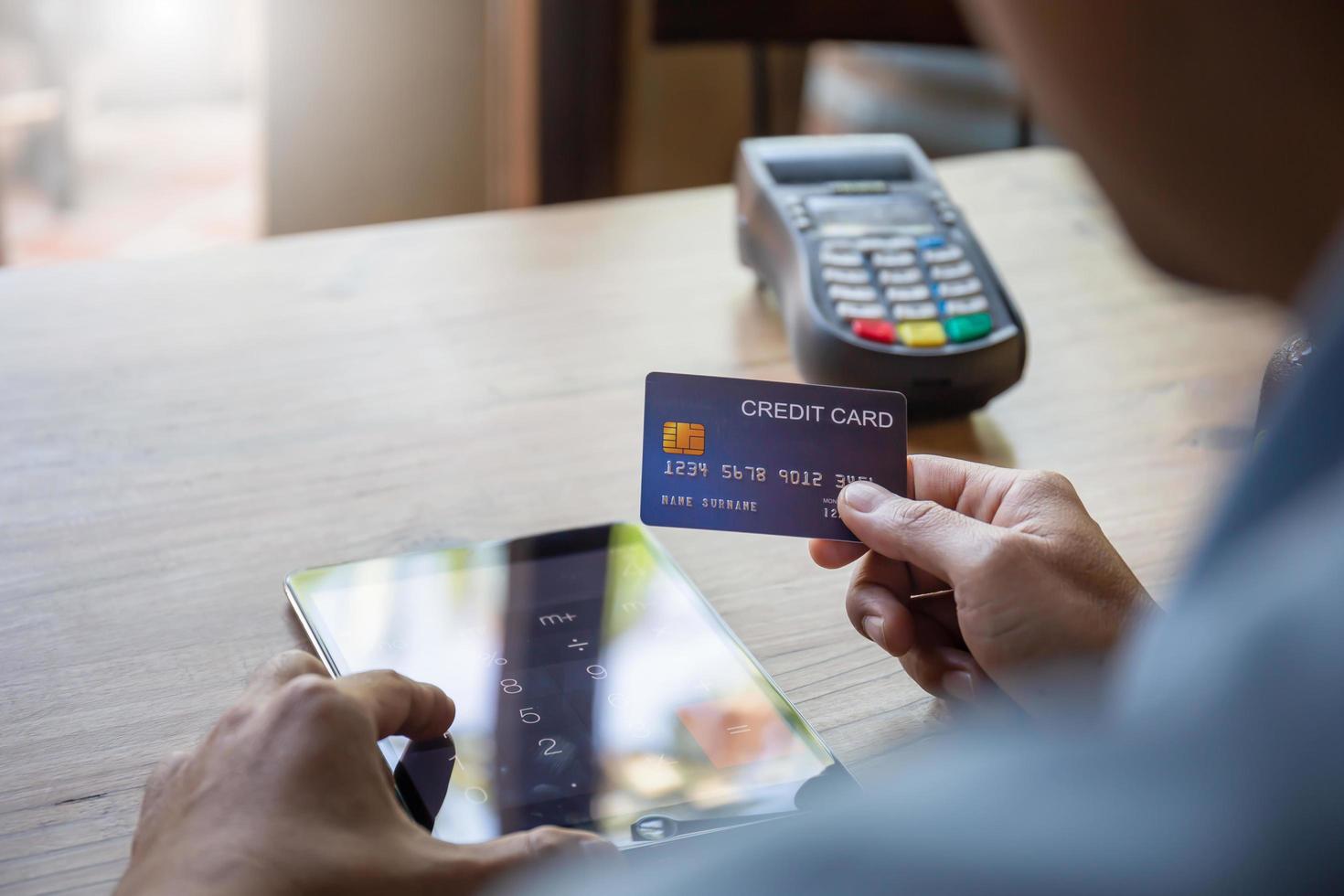 man som håller kreditkort med suddigt en kreditkortsläsare vid bardisken, hand av kunden som betalar med kontaktlöst kreditkort med nfc-teknik. foto
