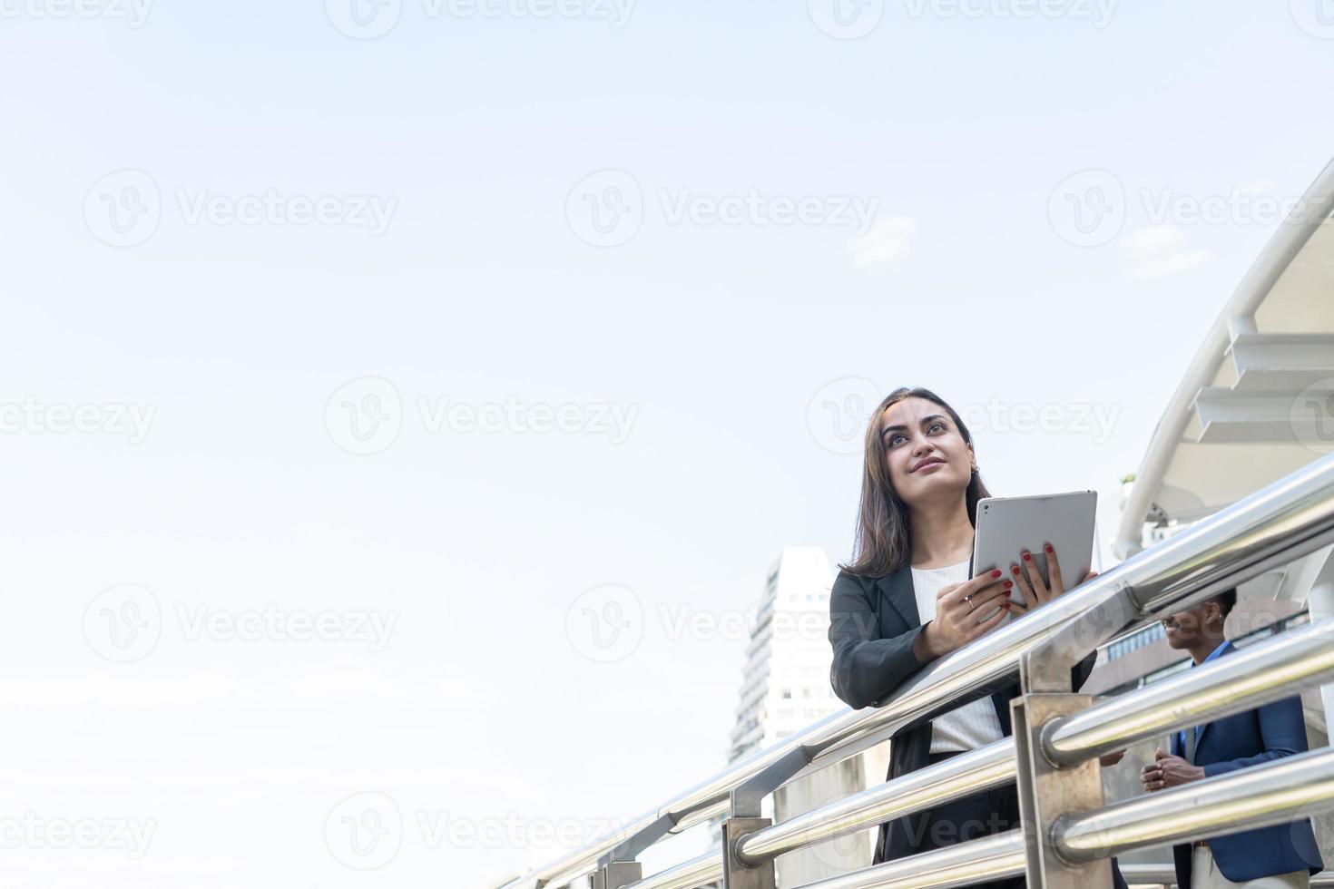 affärskvinna med kommunikationsenhet i staden. framgångsrik kvinnlig bankir använder surfplatta utomhus medan du står nära kontorsbakgrund foto