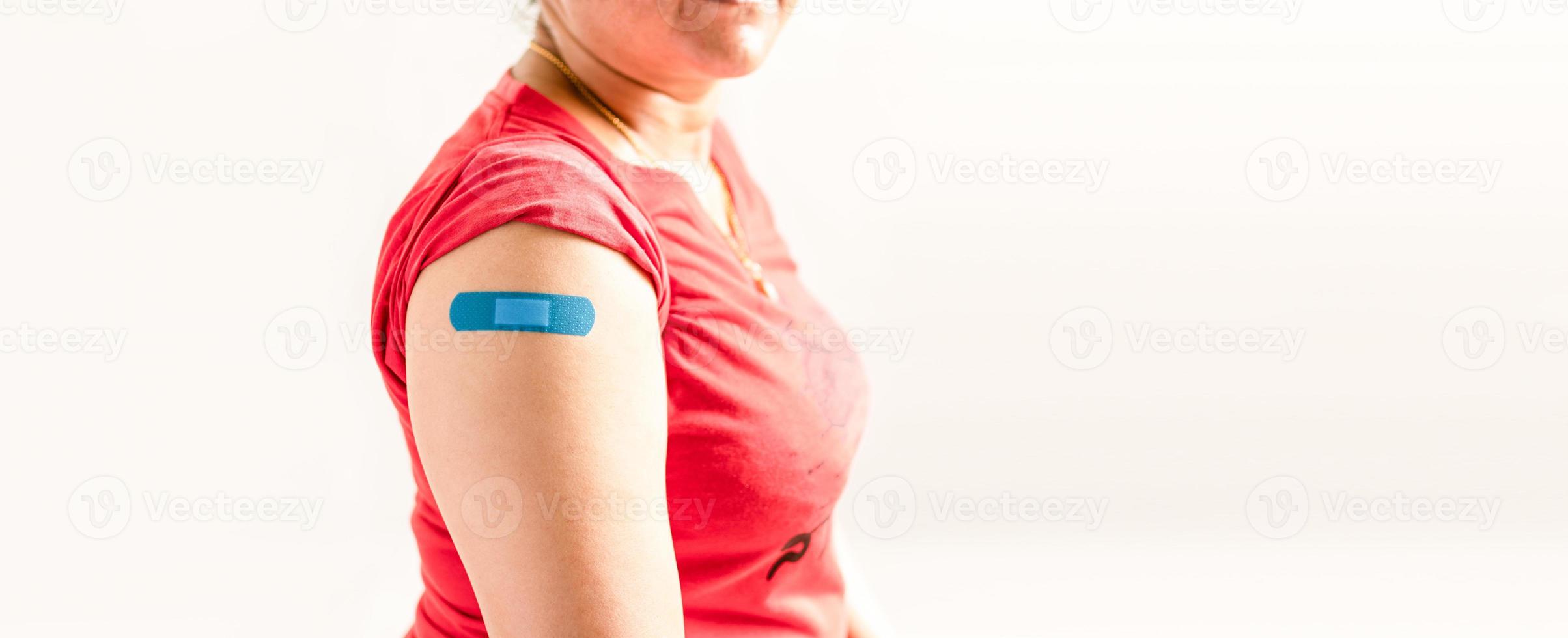 ett blått plåster är fäst på kvinnans arm. koncept för första hjälpen efter vaccination mot coronavirus covid-19 och professionell, medicinsk, nål, blod, cancer. närbild, vit suddig bakgrund foto