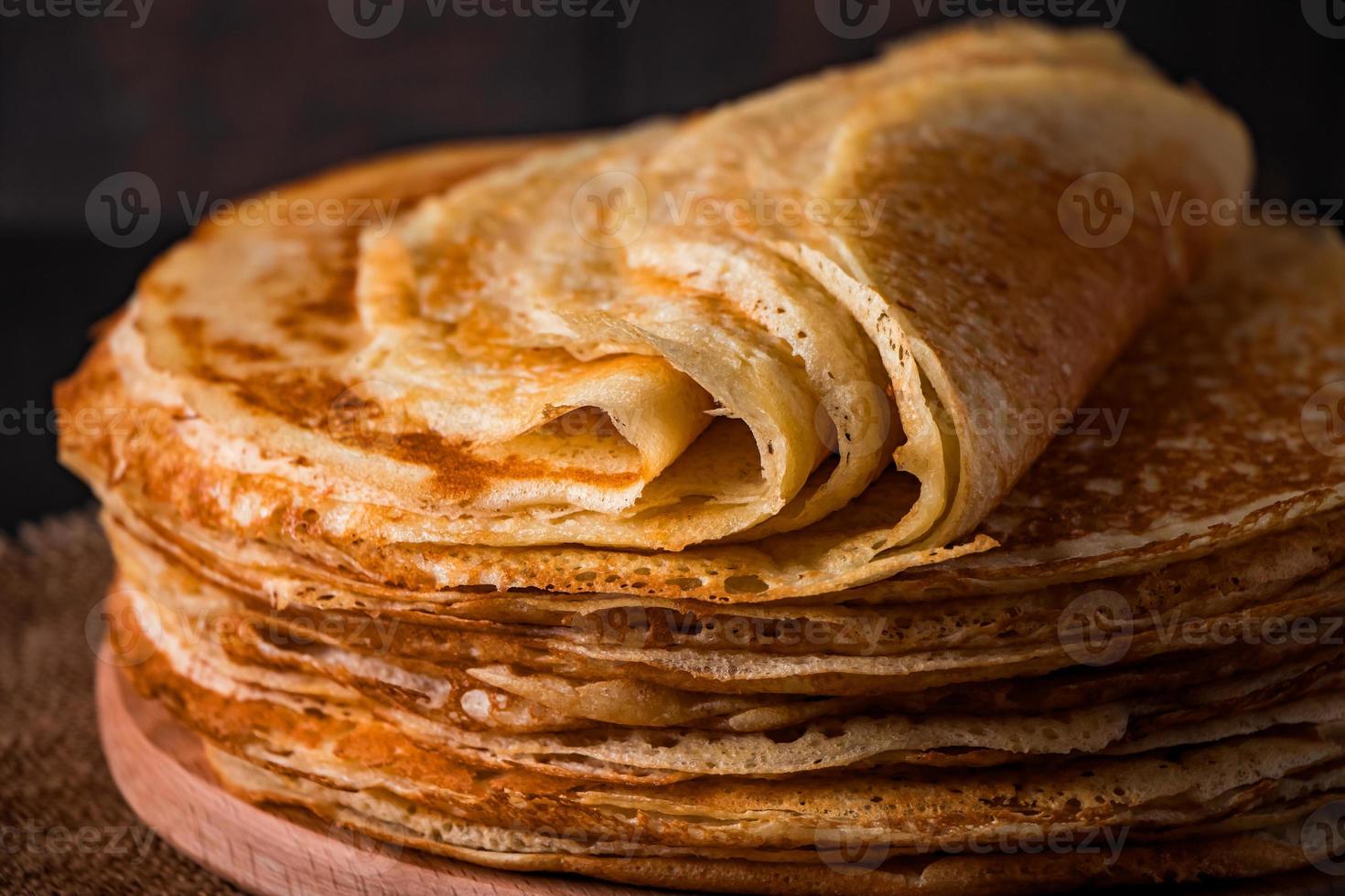 en stapel tunna pannkakor på en mörk träbakgrund. en traditionell maträtt av crepes för semestern maslenitsa. foto