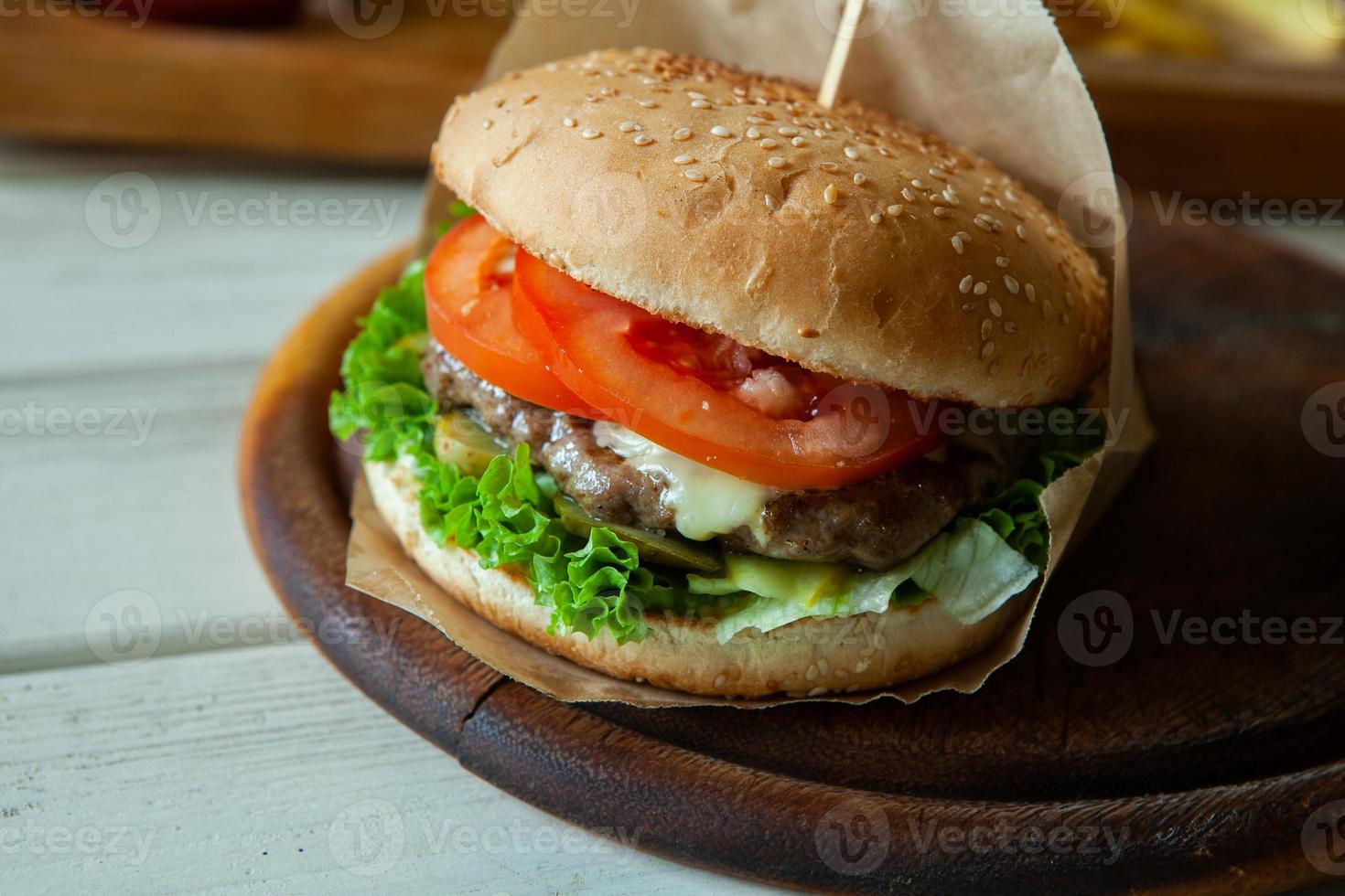 stor välsmakande hamburgare på ett träbord och pommes frites. läcker hamburgare med nötkött, tomat, ost och sallad. foto