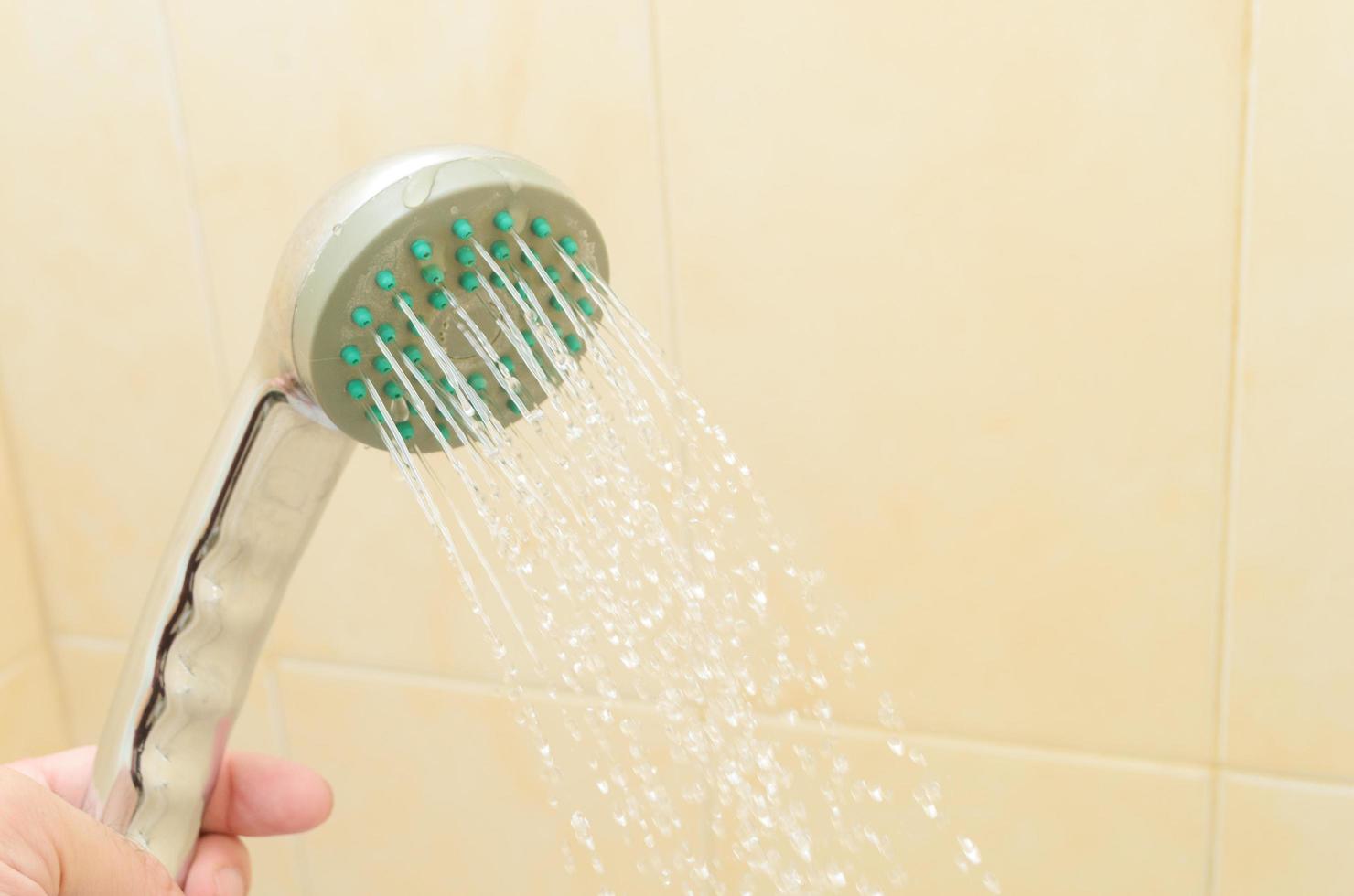 närbild av man som håller duschhuvudet i badrumskabinen. En ström av vatten rinner från duschen. foto