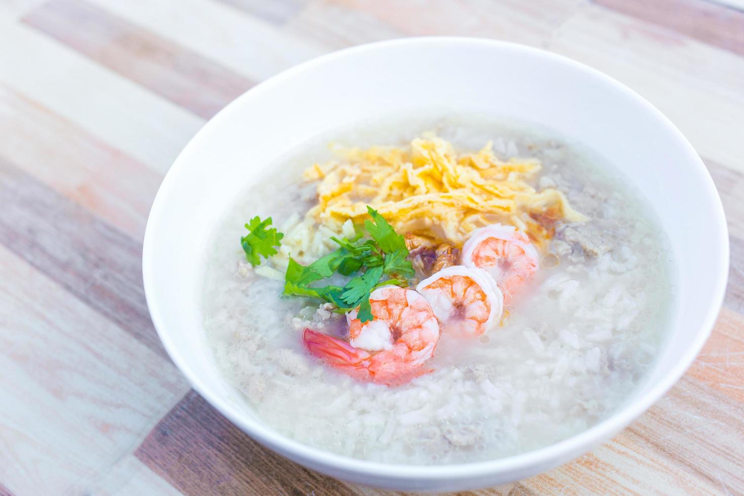 kokt ris med fläsk lades på toppen med hackad omelett, kokta räkor och koriander som en frukostmåltid på morgonen i thailändsk stil medan skålen sattes på träbakgrund. foto