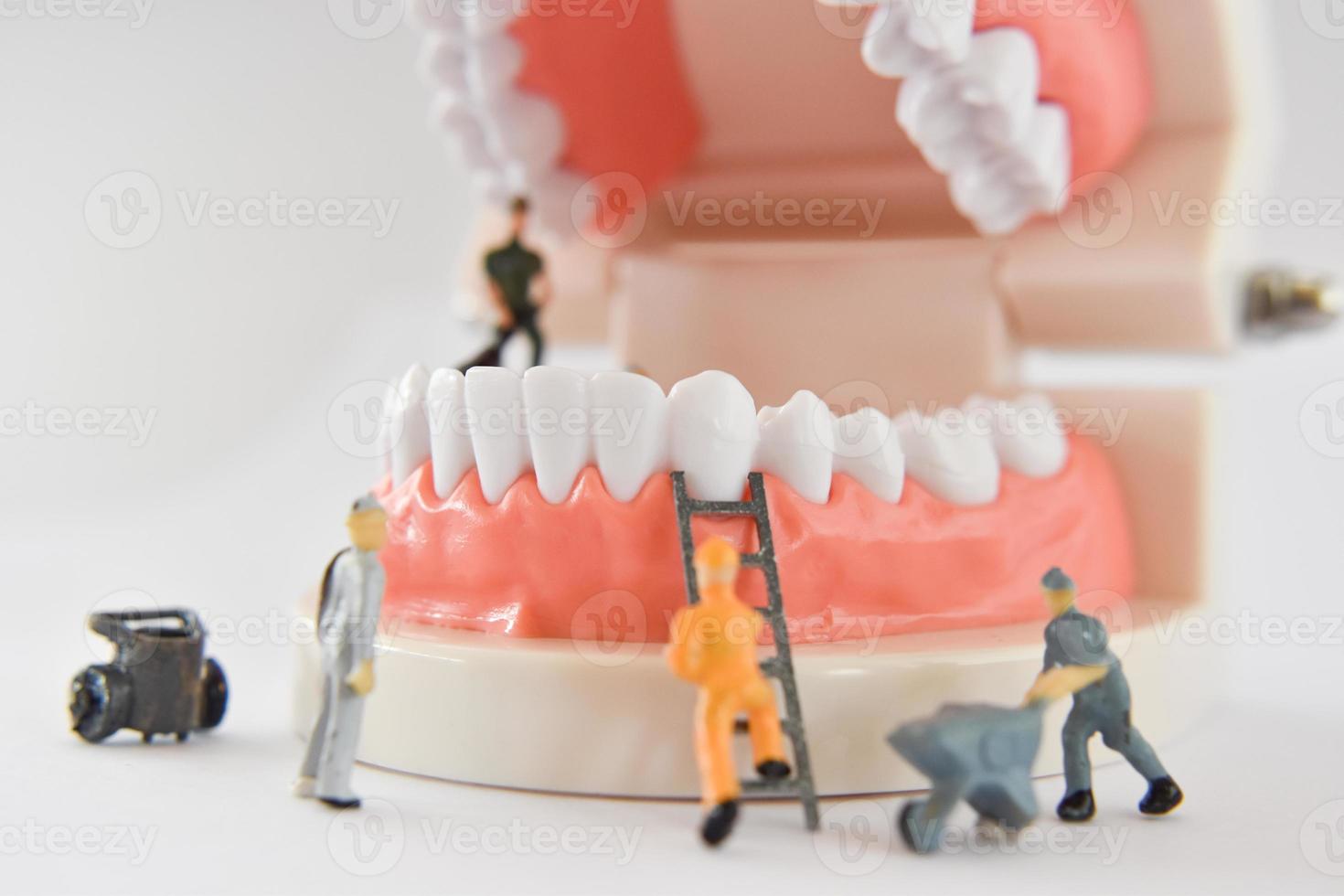 miniatyr människor att reparera en tand eller liten figur arbetare rengöring tand modell som medicinsk och hälsovård. foto