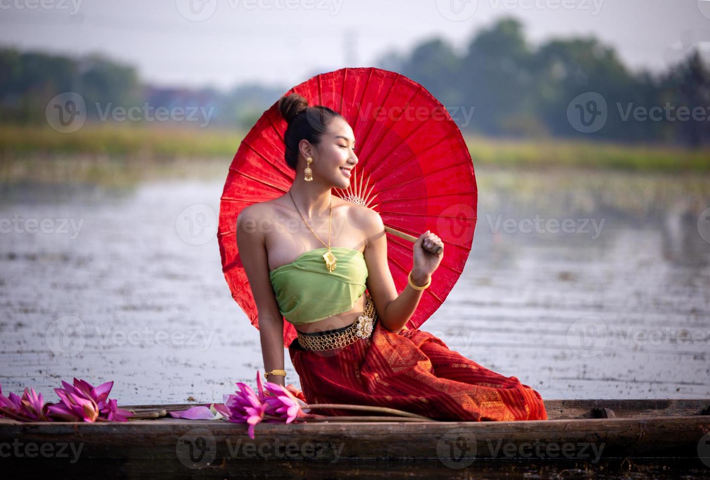 unga asiatiska kvinnor i traditionell klädsel i båten och rosa lotusblommor i dammen. vackra flickor i traditionell kostym. thailändsk flicka i retro thaiklänning, thailändsk flicka i traditionell dräkt foto