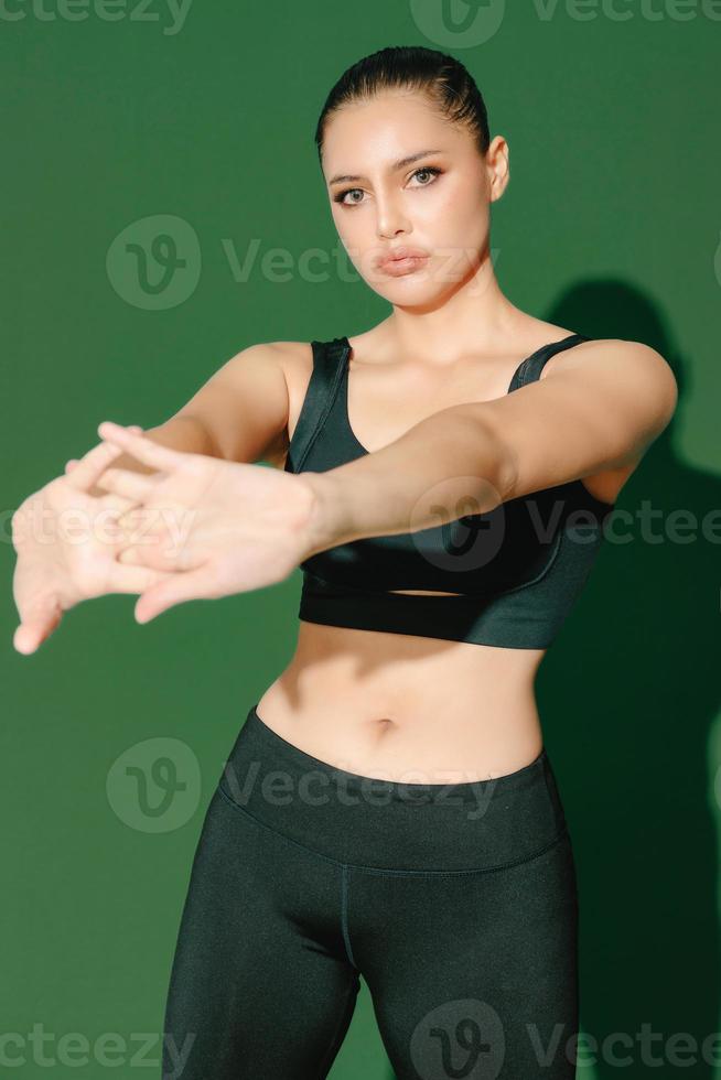 vacker stark glad glad ung asiatisk sportkvinna gör övningar isolerade på grön bakgrund. fitness tjej i sportkläder poserar inomhus. rörelse, styrka och motivation. foto