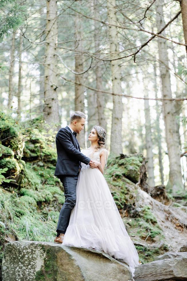 attraktivt par nygifta, lyckliga och glada ögonblick. man och kvinna i festliga kläder sitter på stenarna nära bröllopsdekorationen i boho-stil. ceremoni utomhus. foto