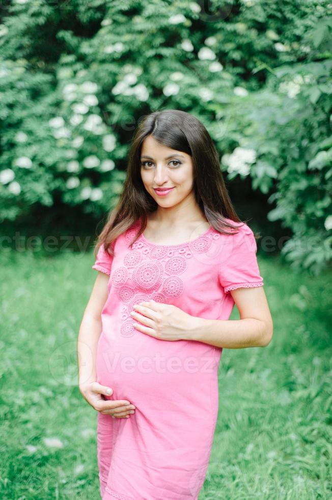 vacker gravid kvinna kopplar av utanför i parken foto