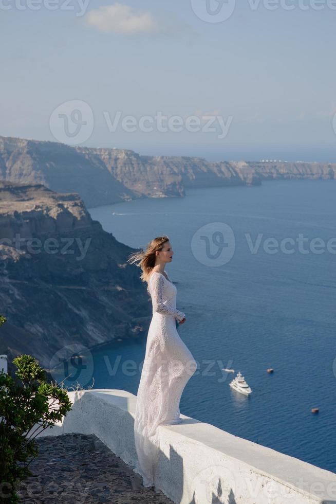 glad kvinna i vit klänning och halmhatt njuter av sin semester på ön santorini. utsikt över Egeiska havet från Oia. europa sommarresmål. grekiska öarna foto