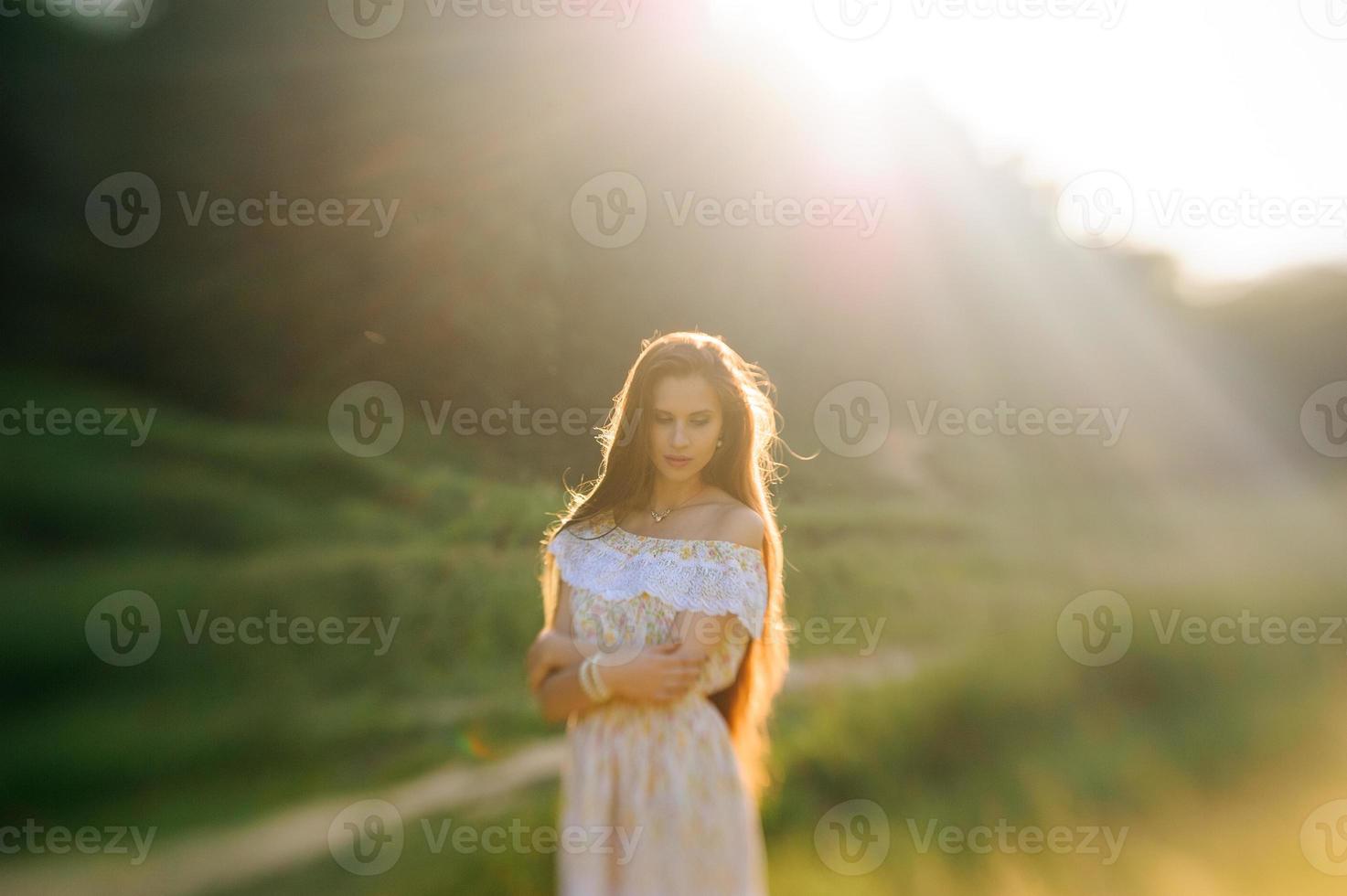 porträtt av en ung vacker flicka i en solklänning. sommarfotosession i parken vid solnedgången. en flicka sitter under ett träd i skuggan. foto