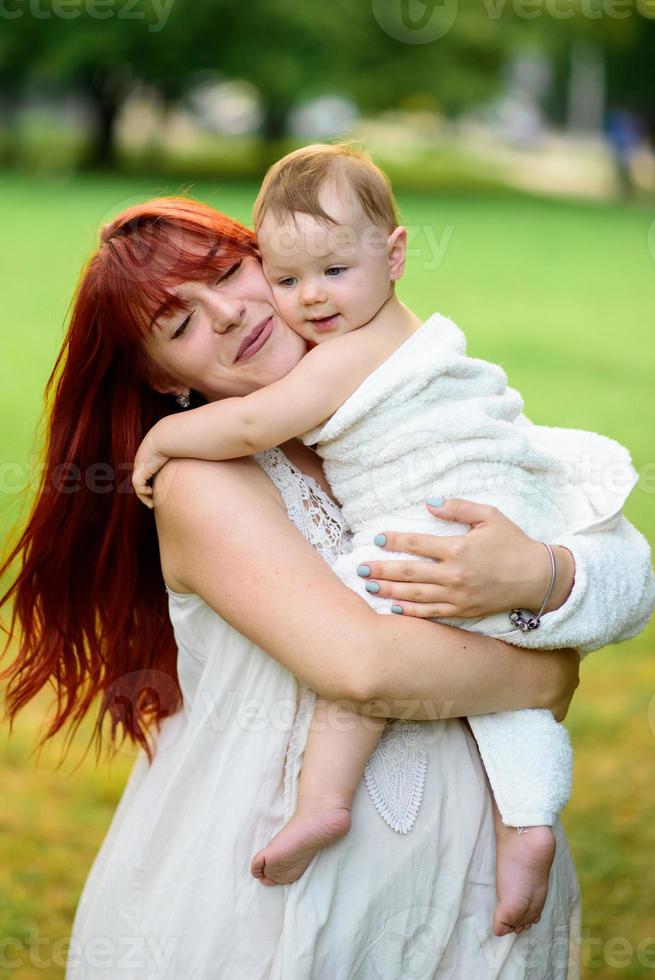 mamma kramar och leker med sin ettåriga dotter inlindad i en handduk efter att ha badat. foto