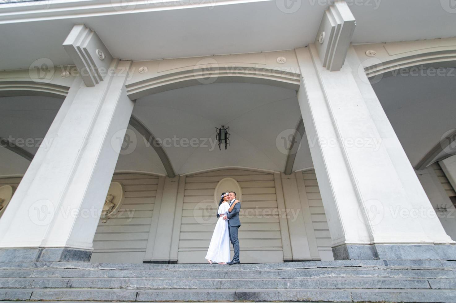 bröllop fotosession på bakgrunden av den gamla byggnaden. brudgummen tittar på sin brud poserar. rustik eller boho bröllopsfotografering. foto