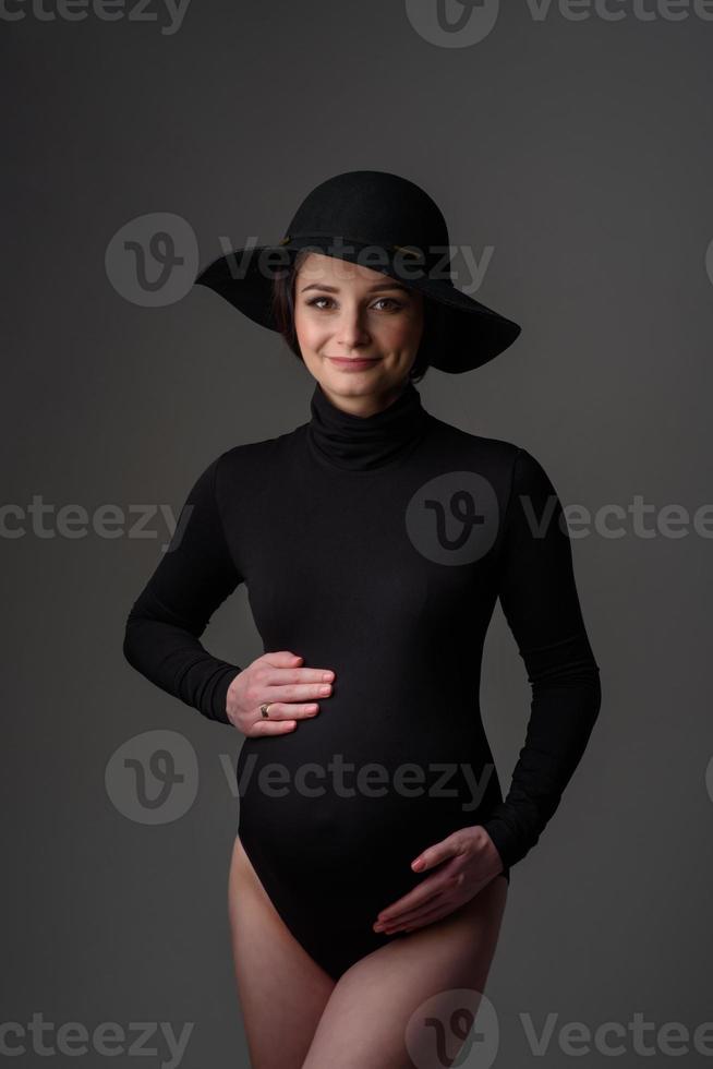 ung vacker gravid kvinna i svart bodysuit och hatt. foto