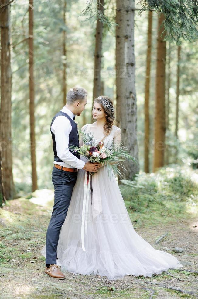 attraktivt par nygifta, lyckliga och glada ögonblick. man och kvinna i festliga kläder sitter på stenarna nära bröllopsdekorationen i boho-stil. ceremoni utomhus. foto