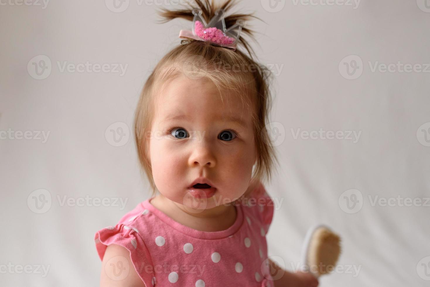 liten flicka 6 månader gammal med en kam i handen på en vit bakgrund. foto