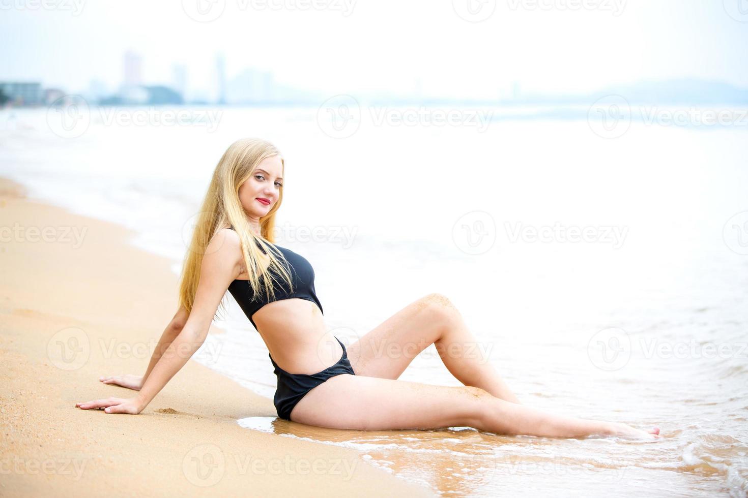 vacker blond kvinna på svart bikini njuta av sommaren på stranden. foto