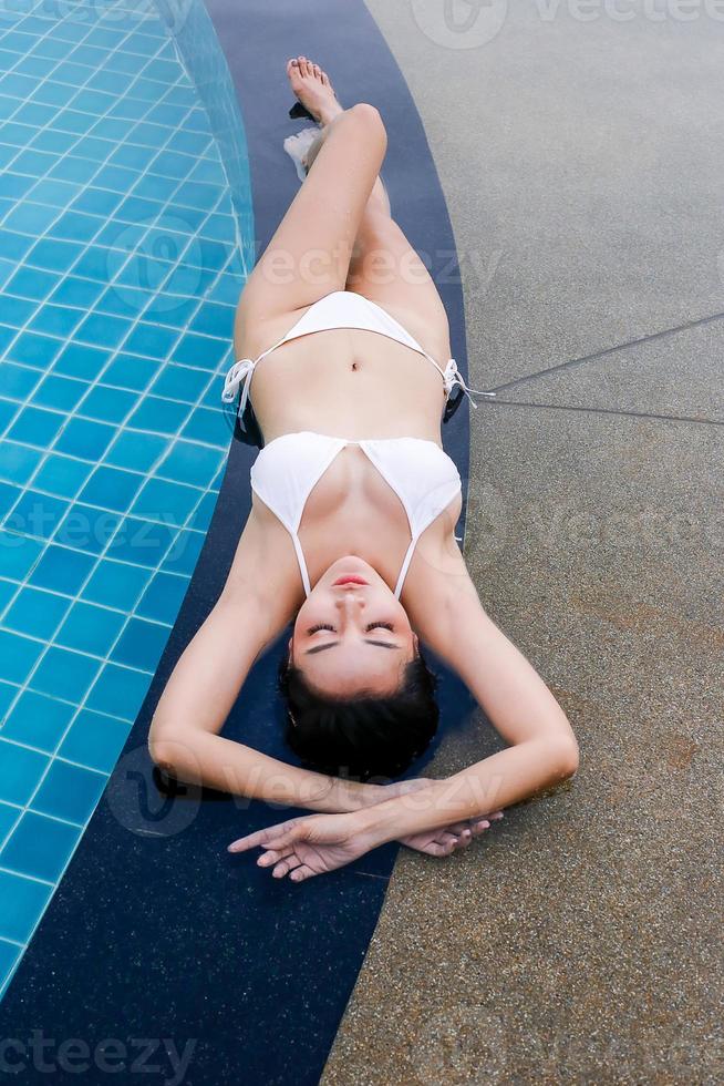 ung kvinna njuter och kopplar av vid poolen. smal ung tjejmodell i vit bikini vid poolen. foto