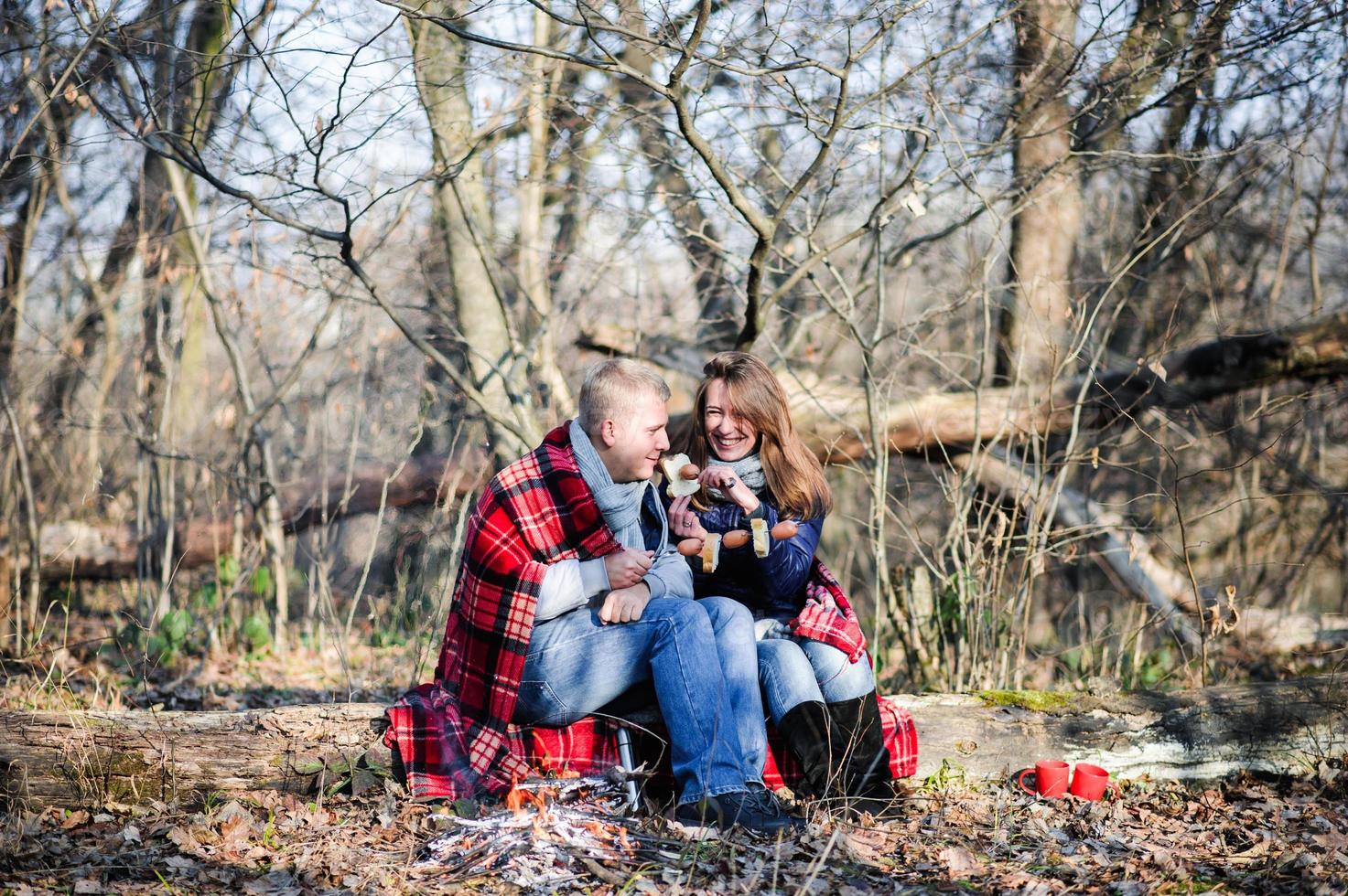 två unga backpackers sitter på huk på snödriva och pratar medan de värmer händerna över eld foto