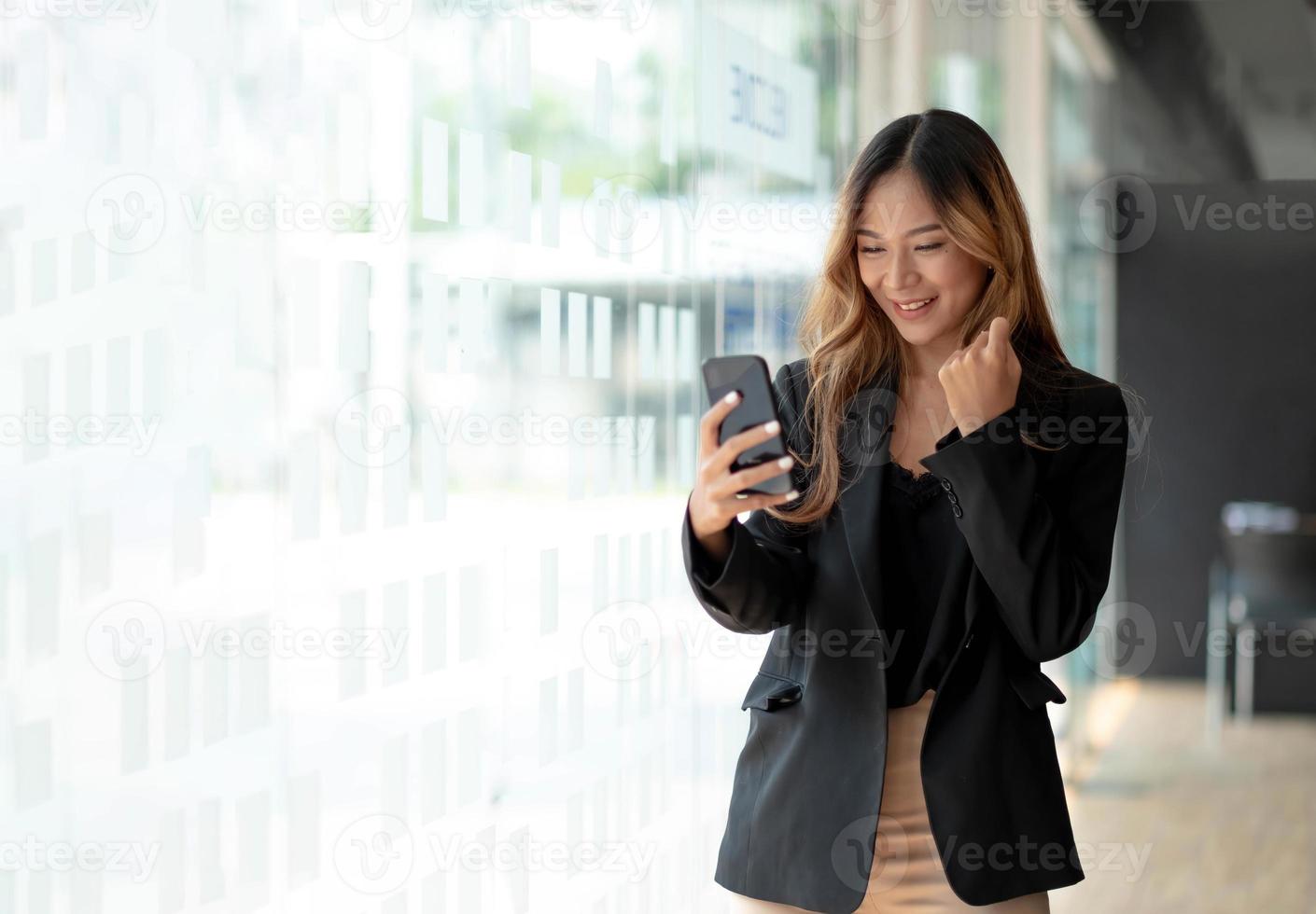 vacker asiatisk kvinna som använder smartphone, spännande och firar med goda nyheter om framgångsrika företag. småföretag startkoncept. foto