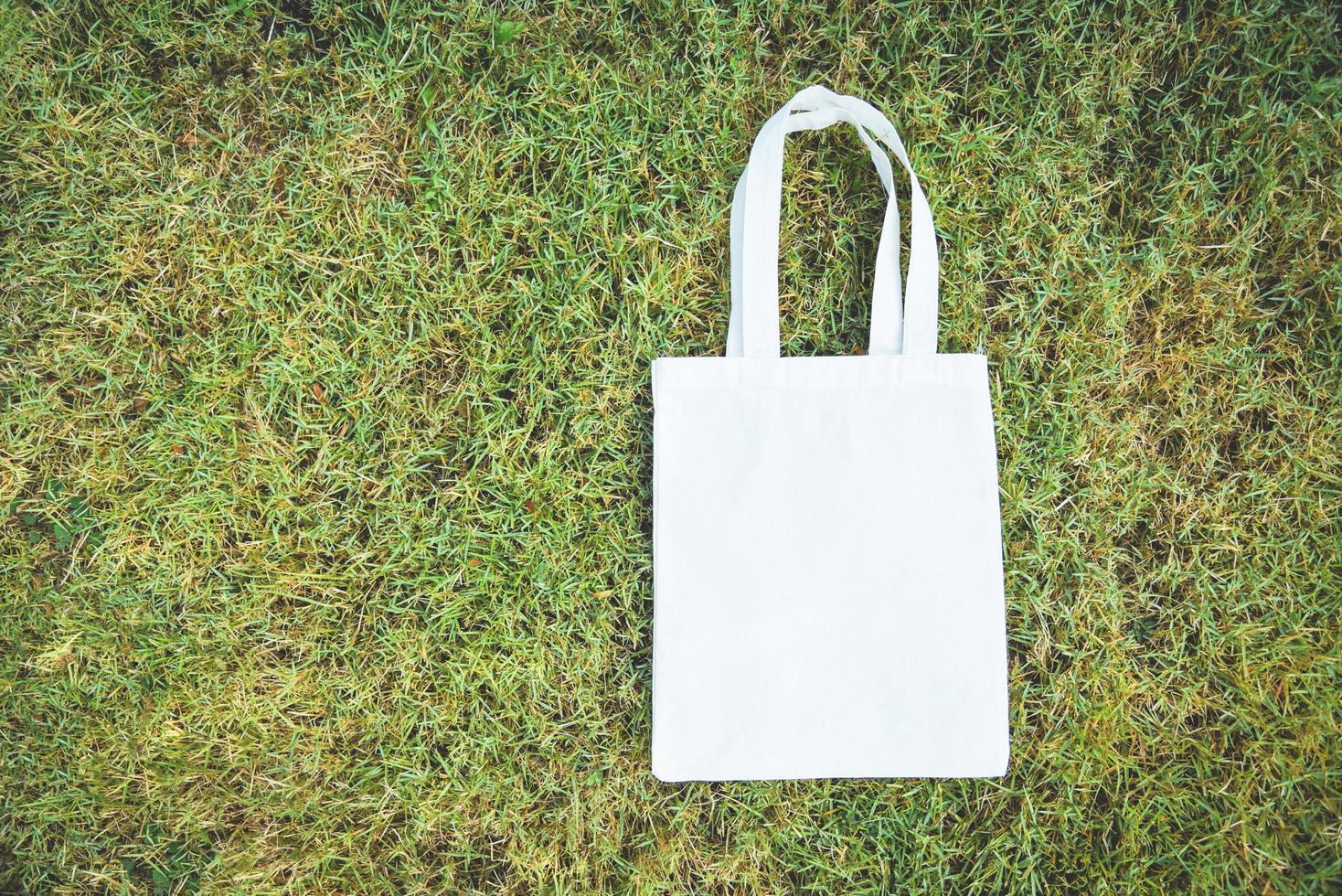 vit tote canvas tyg eko-påse tyg shoppingsäck på grönt gräs bakgrund noll avfall använd mindre plast säg nej plastpåse föroreningsproblem foto