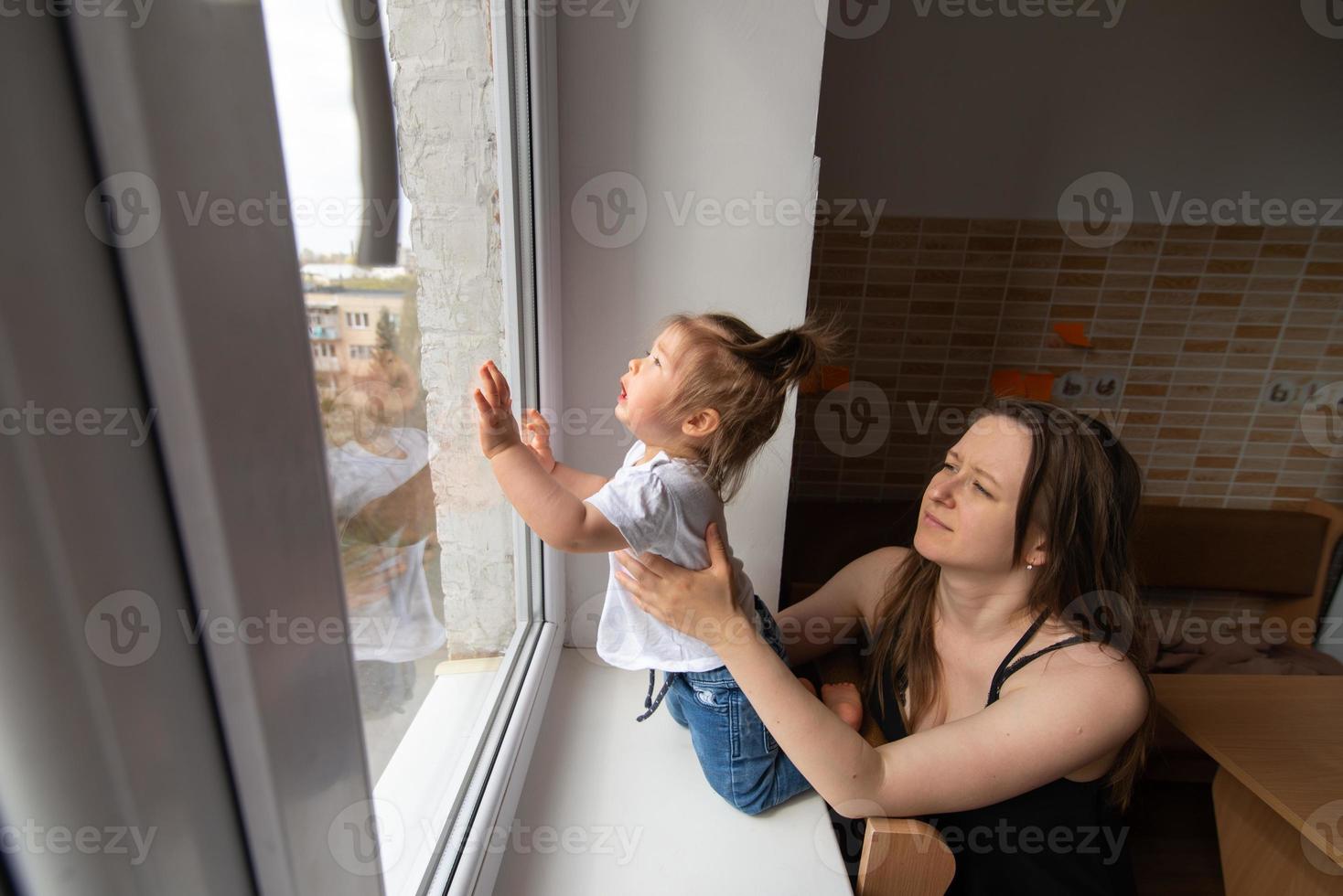 liten flicka tittar ut genom fönstret och frågar utanför under karantän orsakad av coronavirus. foto